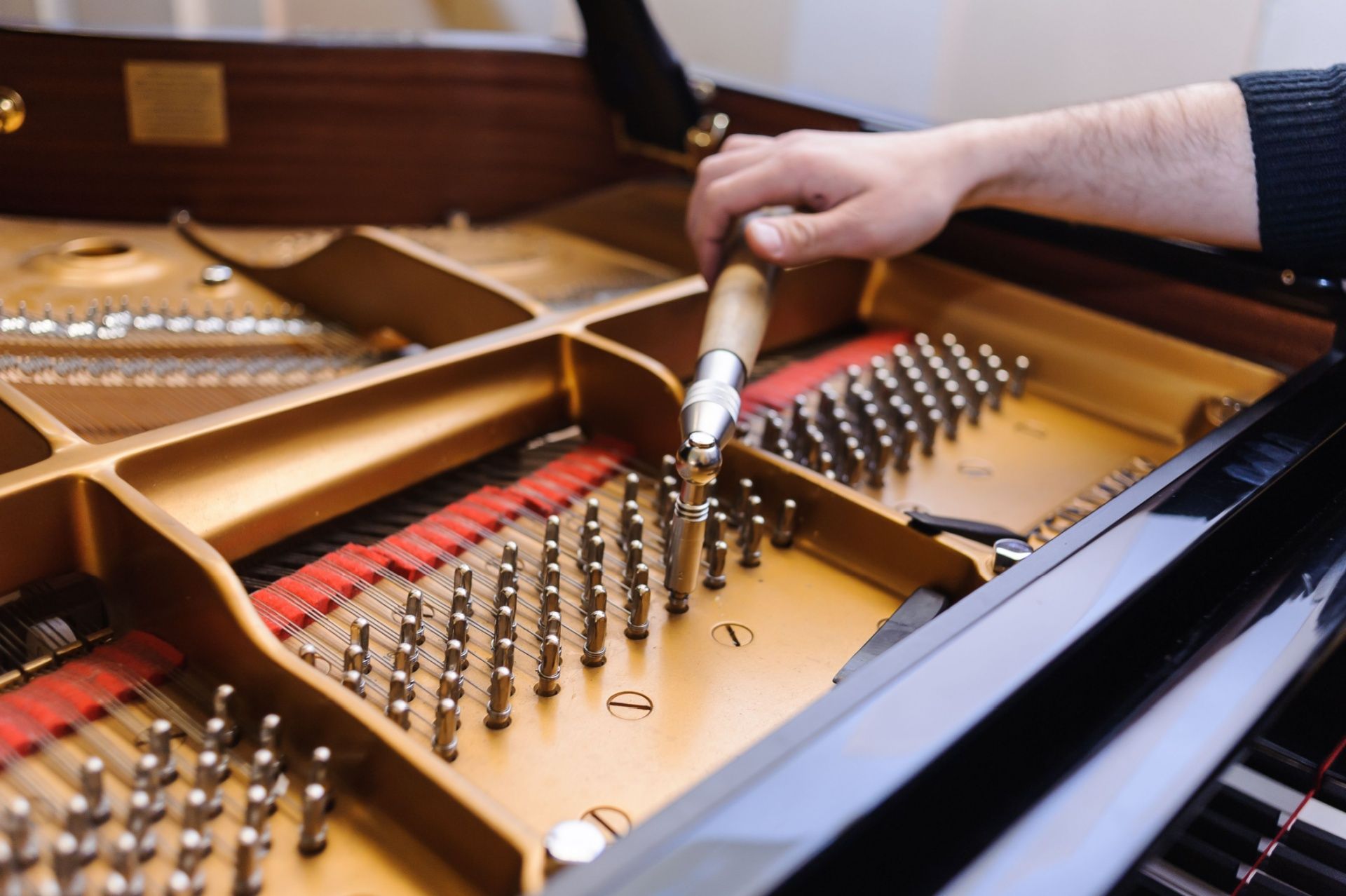 A person tuning a grand piano with a tuning lever, inside view of the instrument's strings and pins.