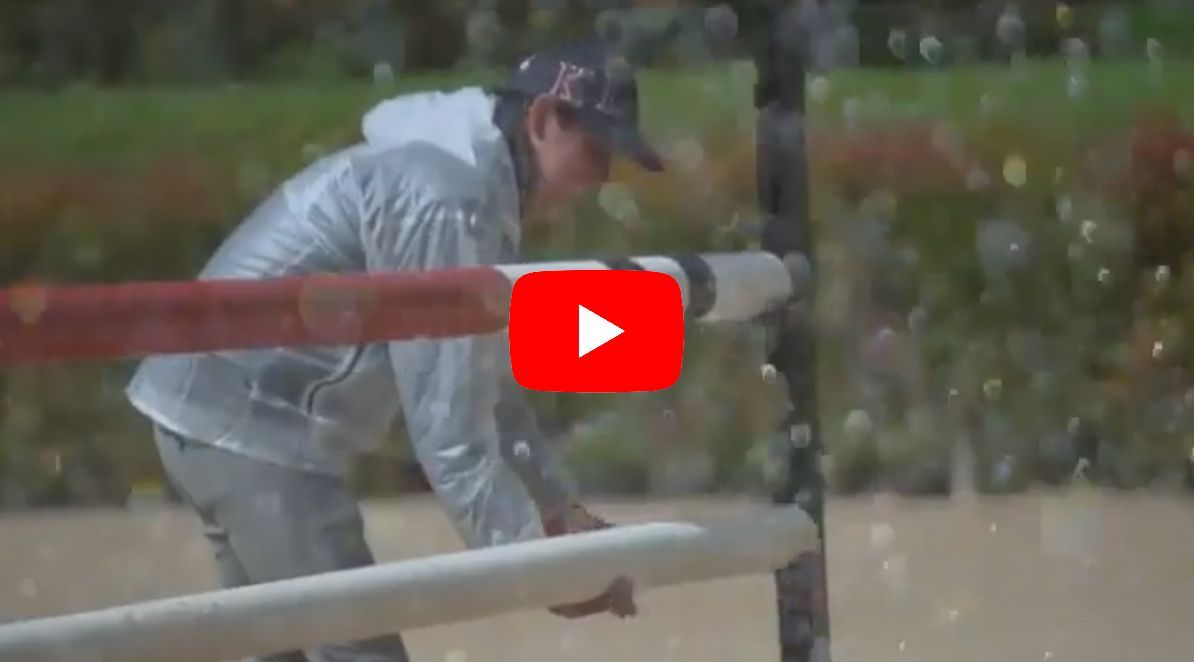 A person in rain gear is adjusting a fence post during a rainy equestrian event.