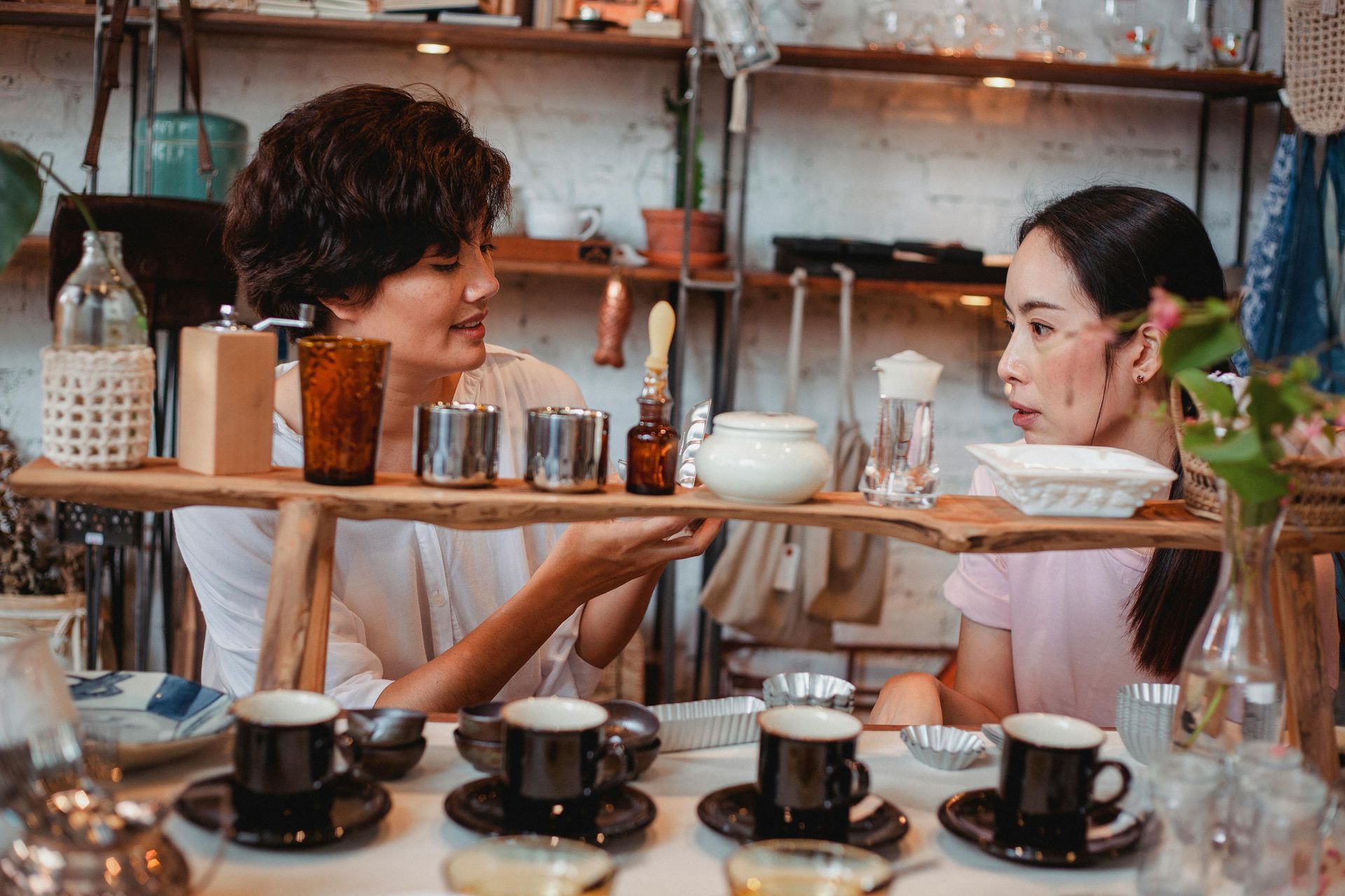 Two women are sitting at a table with coffee cups and saucers.