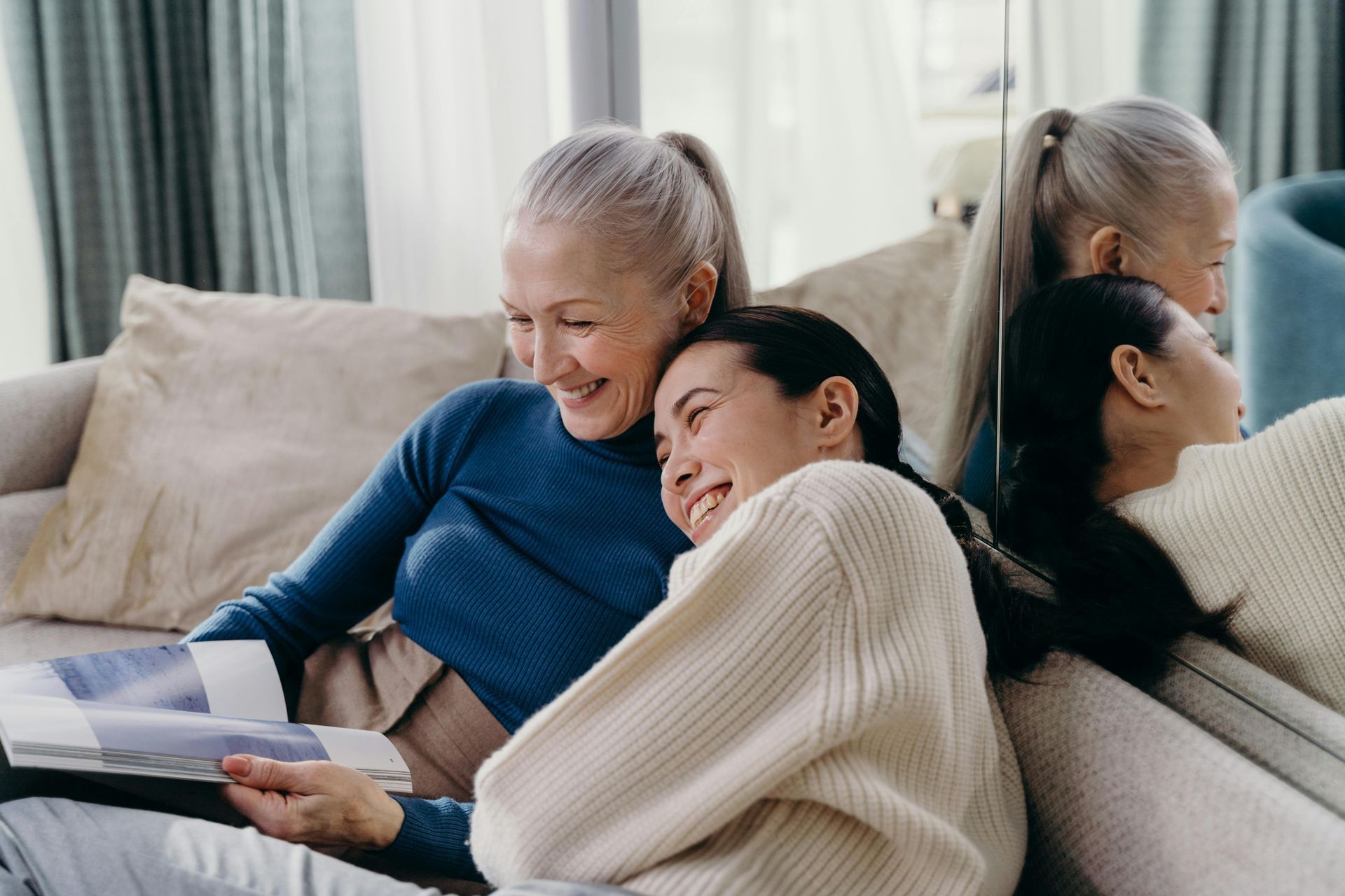 Two women are sitting on a couch looking at a magazine.