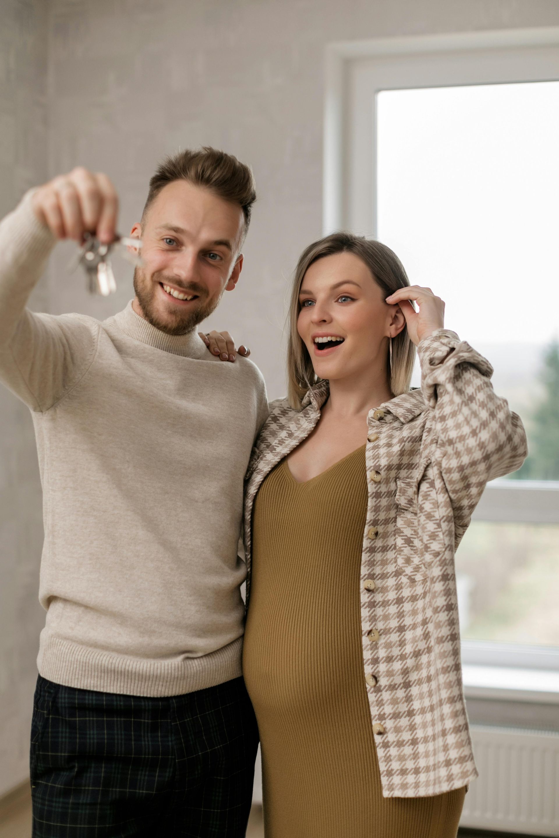 A man and a pregnant woman are holding keys to their new home.
