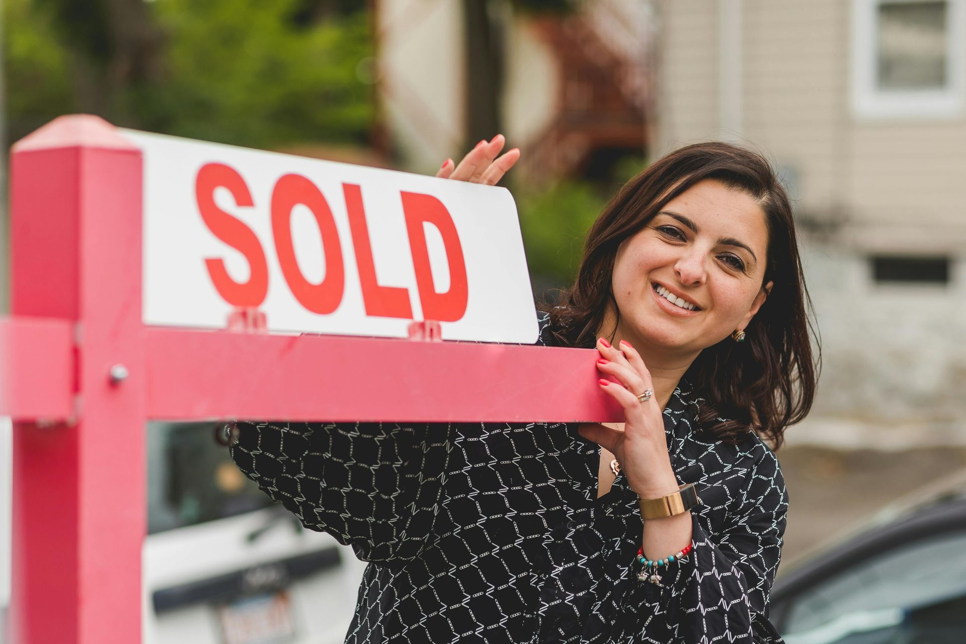 A woman is holding a sold sign in front of a house.