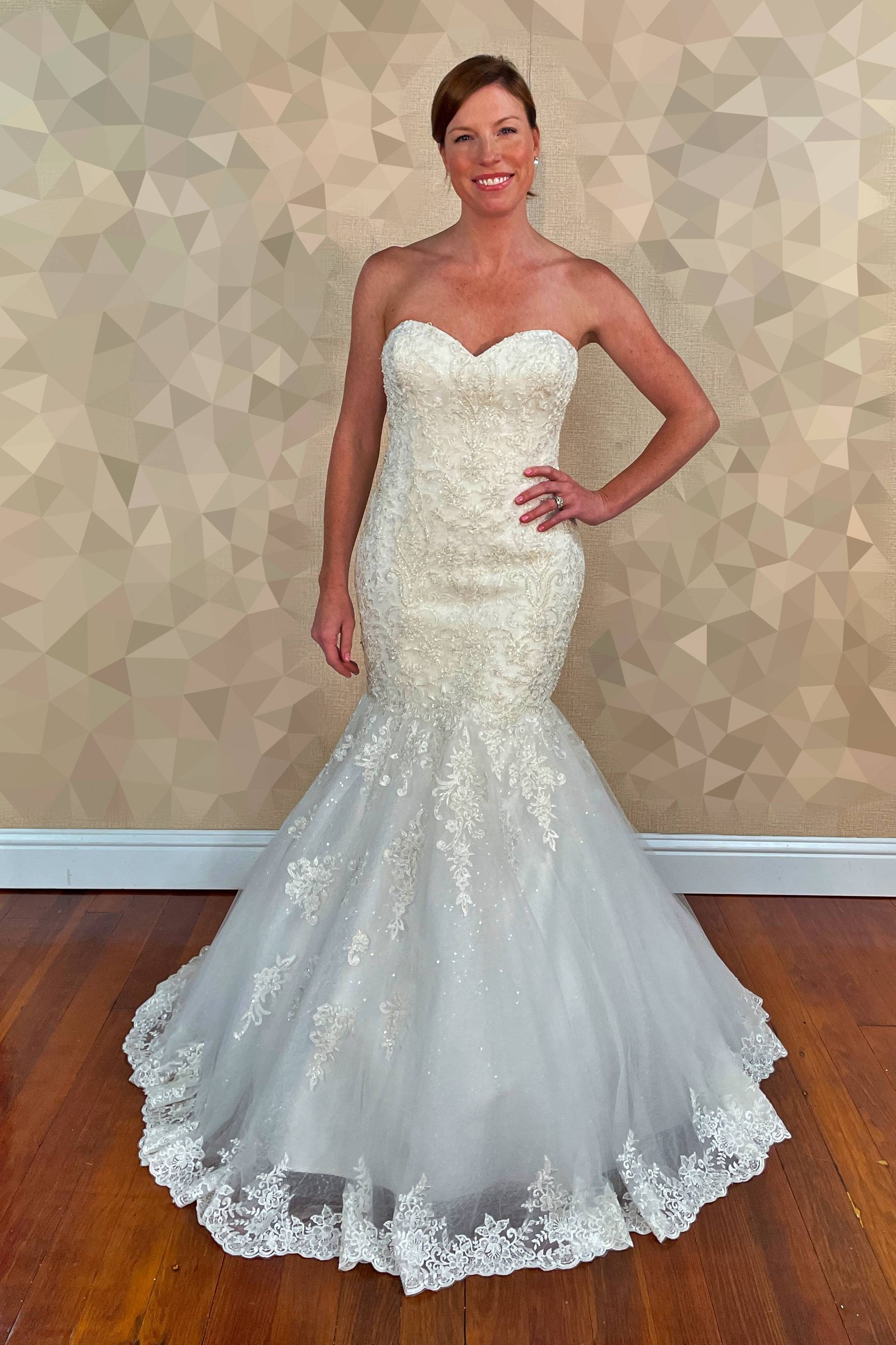 Woman in a white, beaded strapless mermaid wedding dress, smiling, standing indoors near a geometric wall.