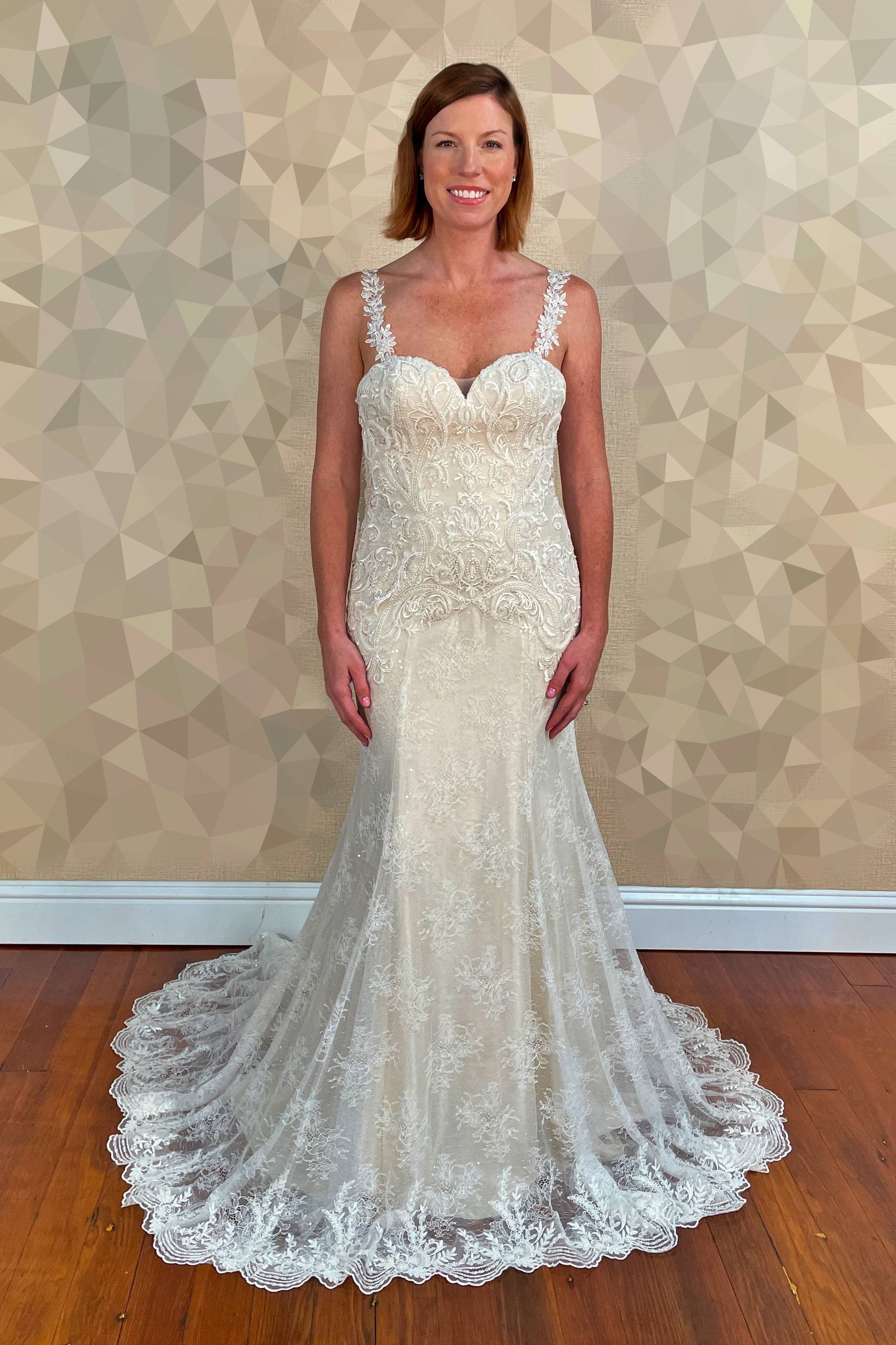 Woman wearing a beaded ivory mermaid wedding dress with a lace train, standing indoors.
