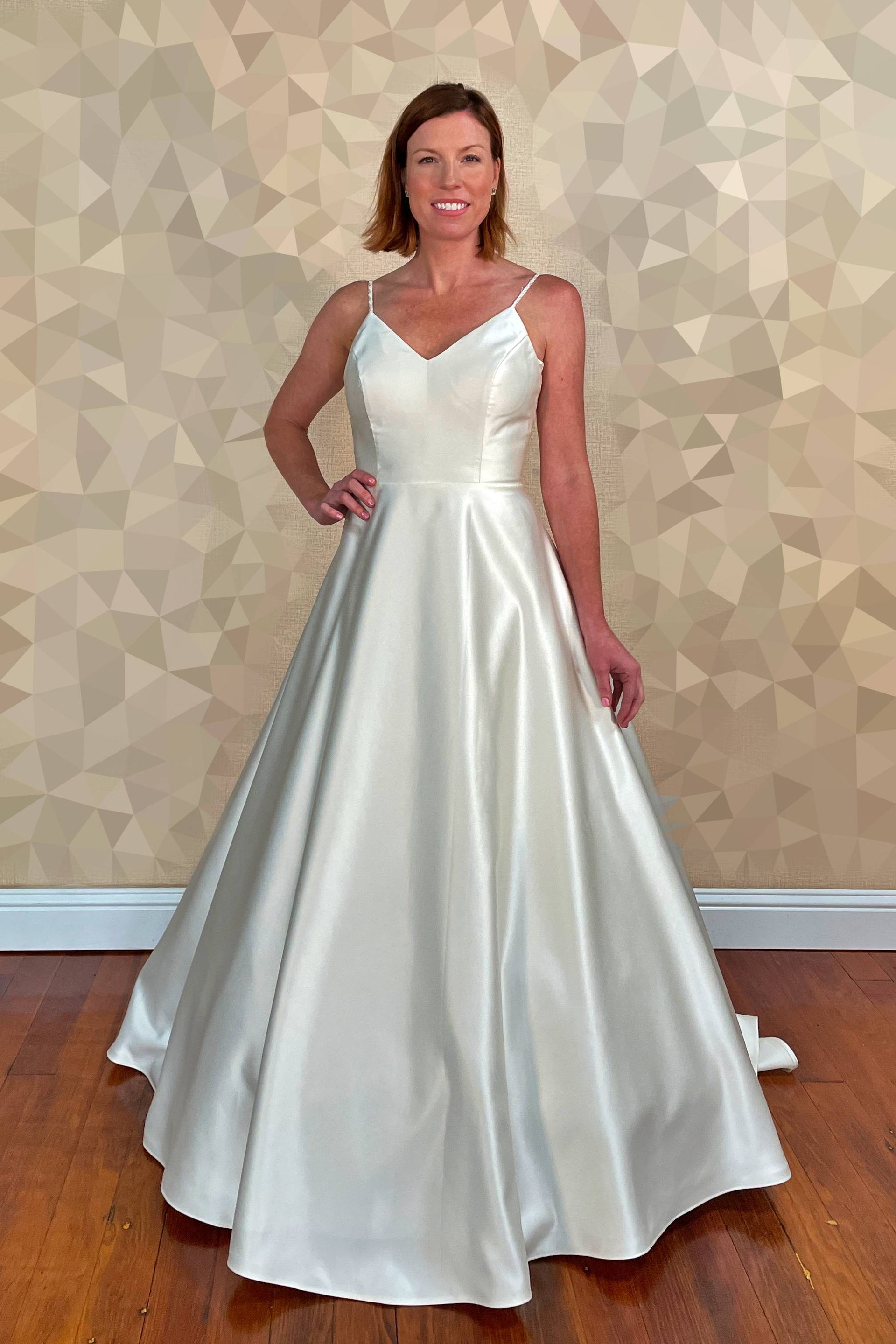 Woman in white satin wedding gown, posing indoors.