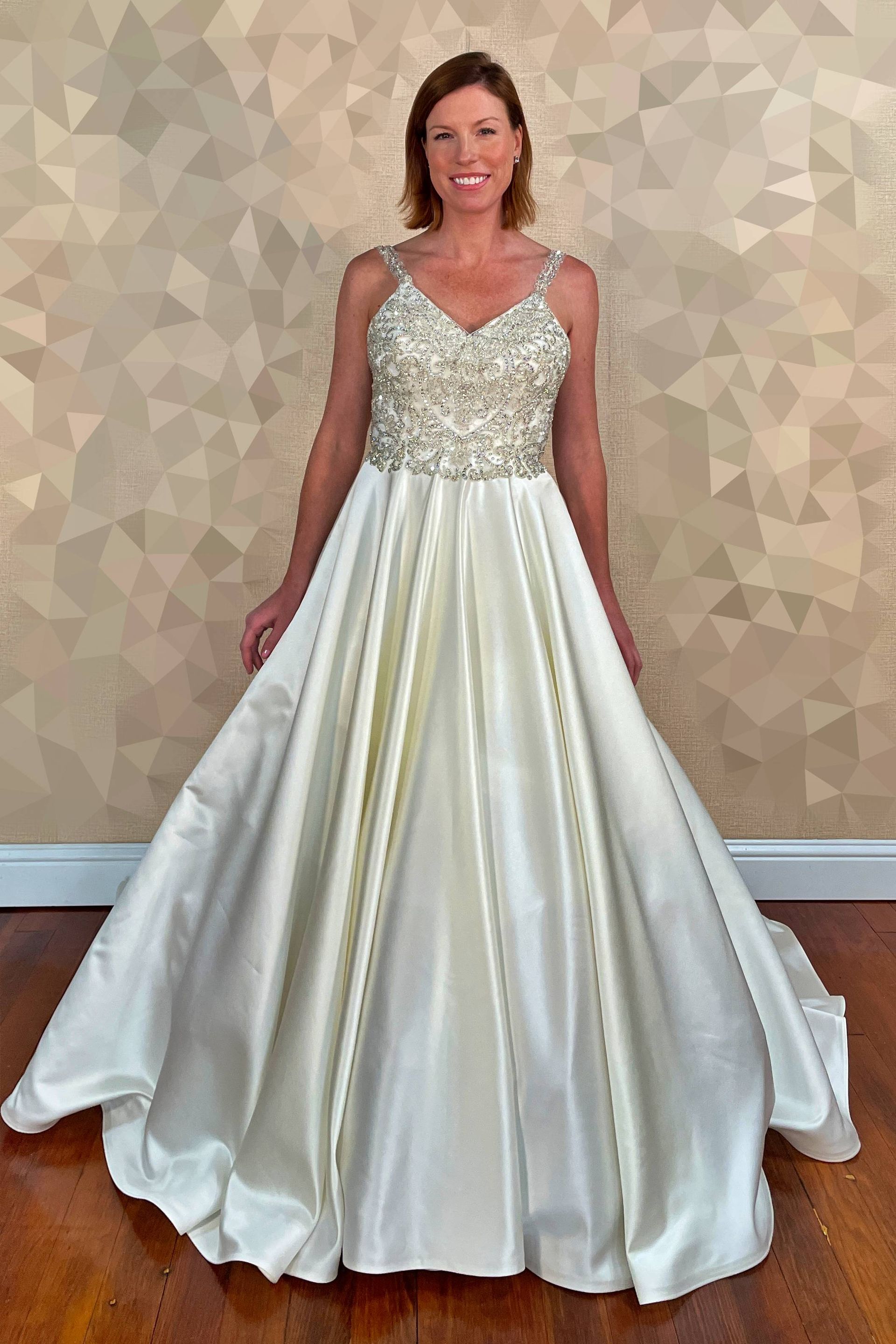 Woman wearing a white, floor-length gown with a jeweled bodice, standing in a room.