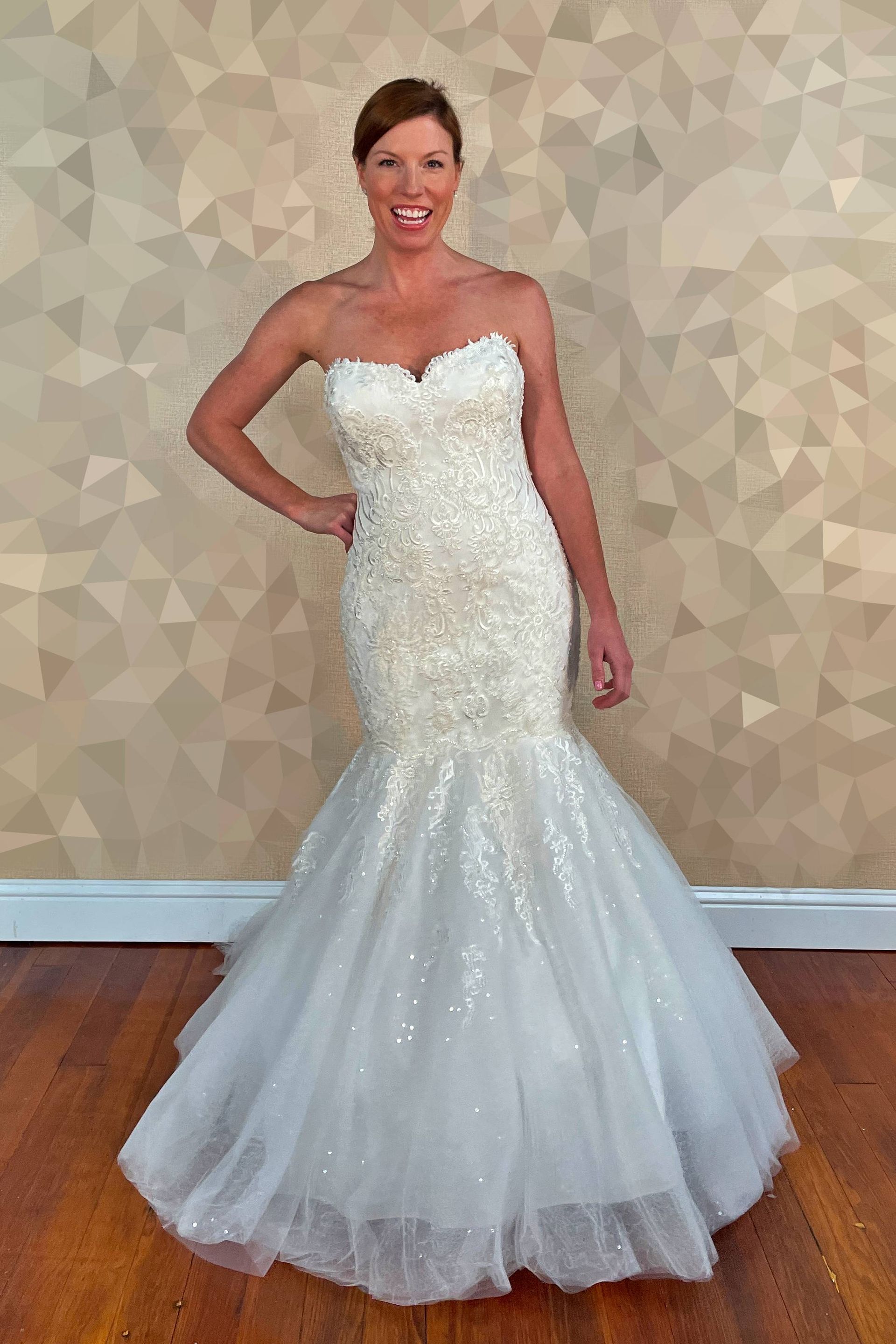 Woman in a strapless white beaded wedding dress, smiling, posed indoors.