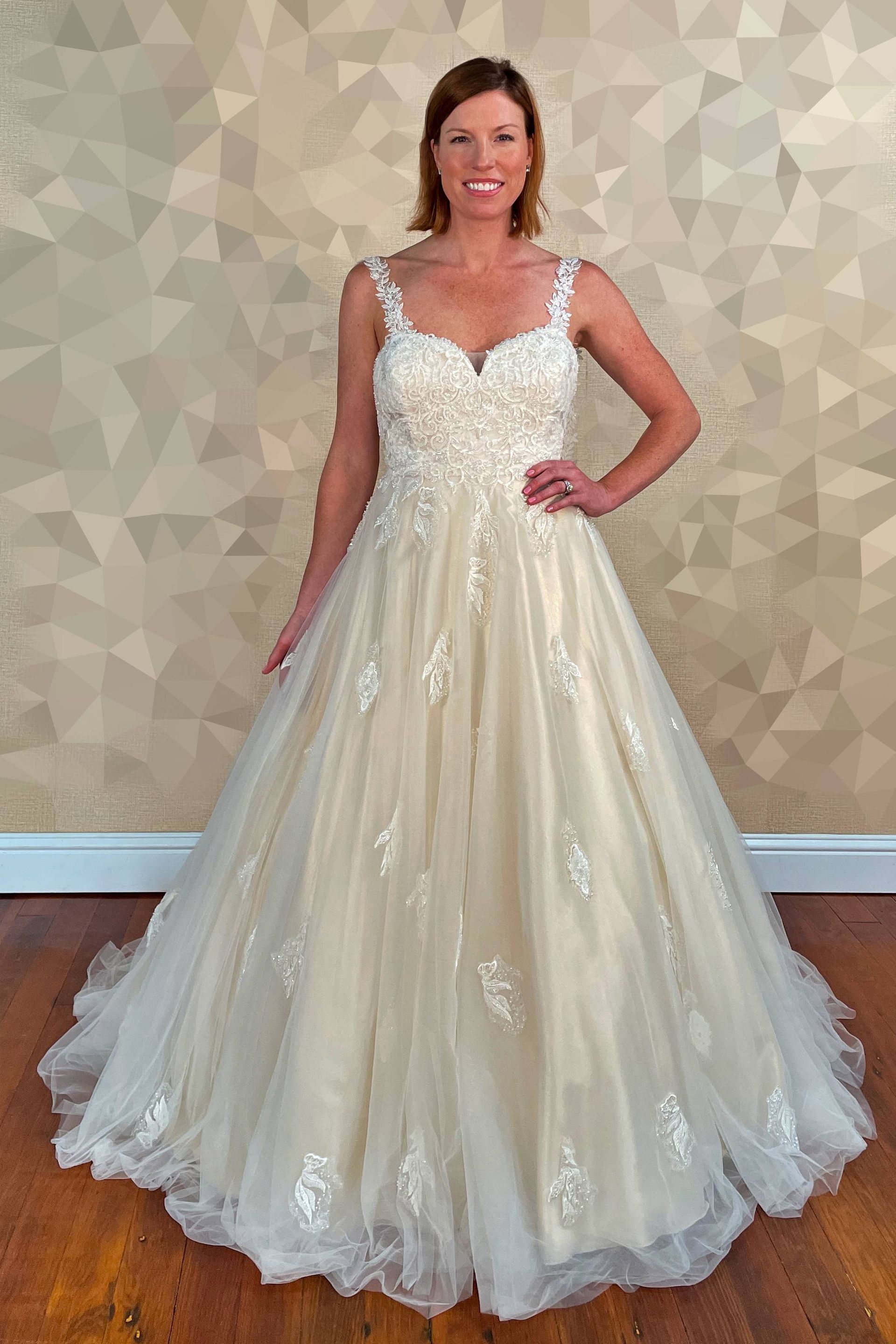 Woman in a wedding gown smiles. She stands in a room with a patterned wall.