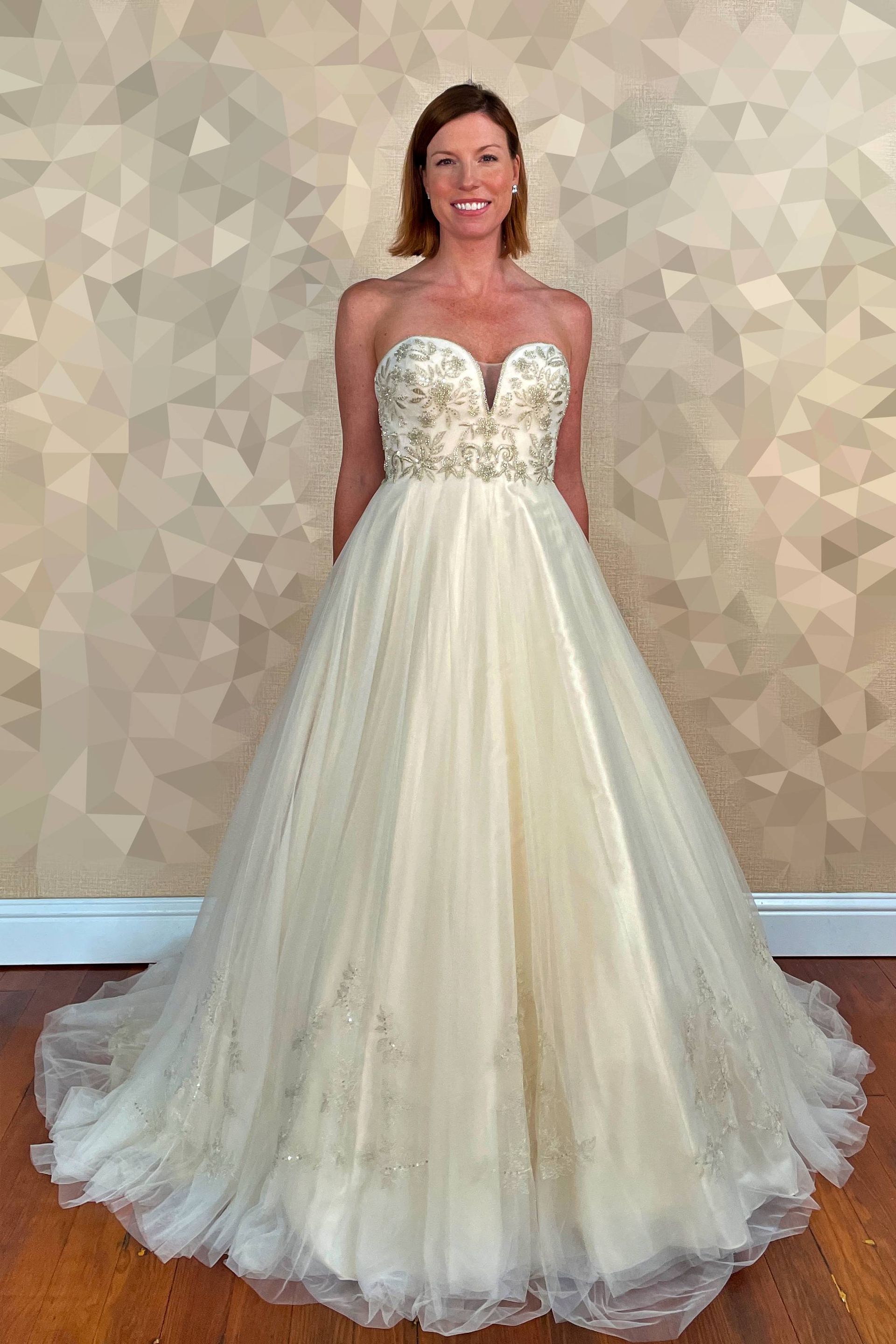 Woman in a strapless ivory wedding gown with beaded bodice, smiling against a patterned wall.