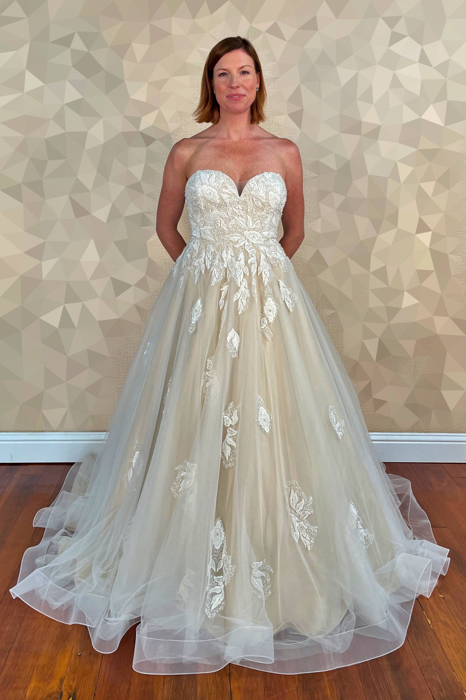 Woman wearing a strapless ivory wedding gown with floral embellishments; standing.