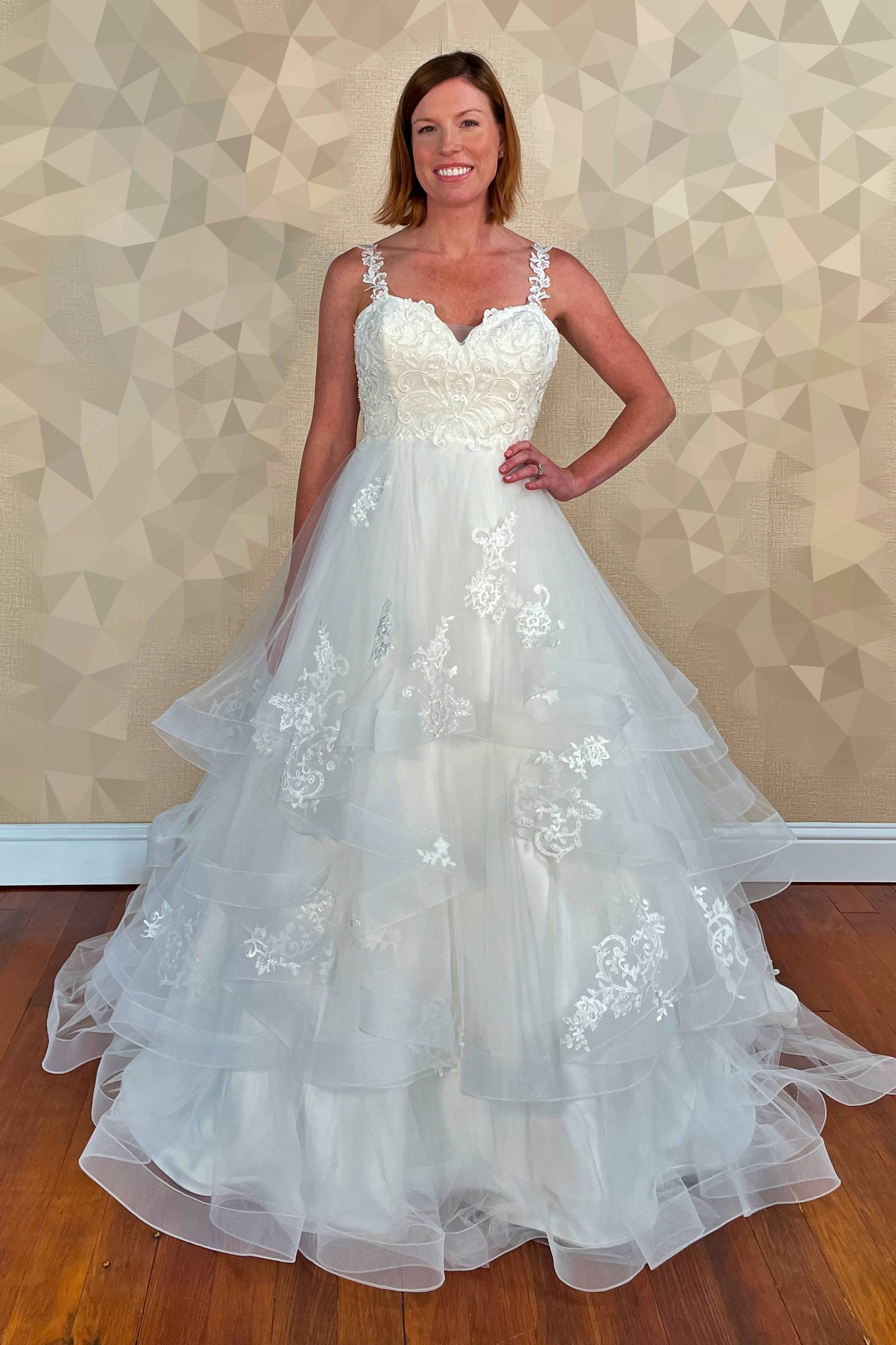 Woman in a white wedding dress with lace details, posing indoors, smiling.