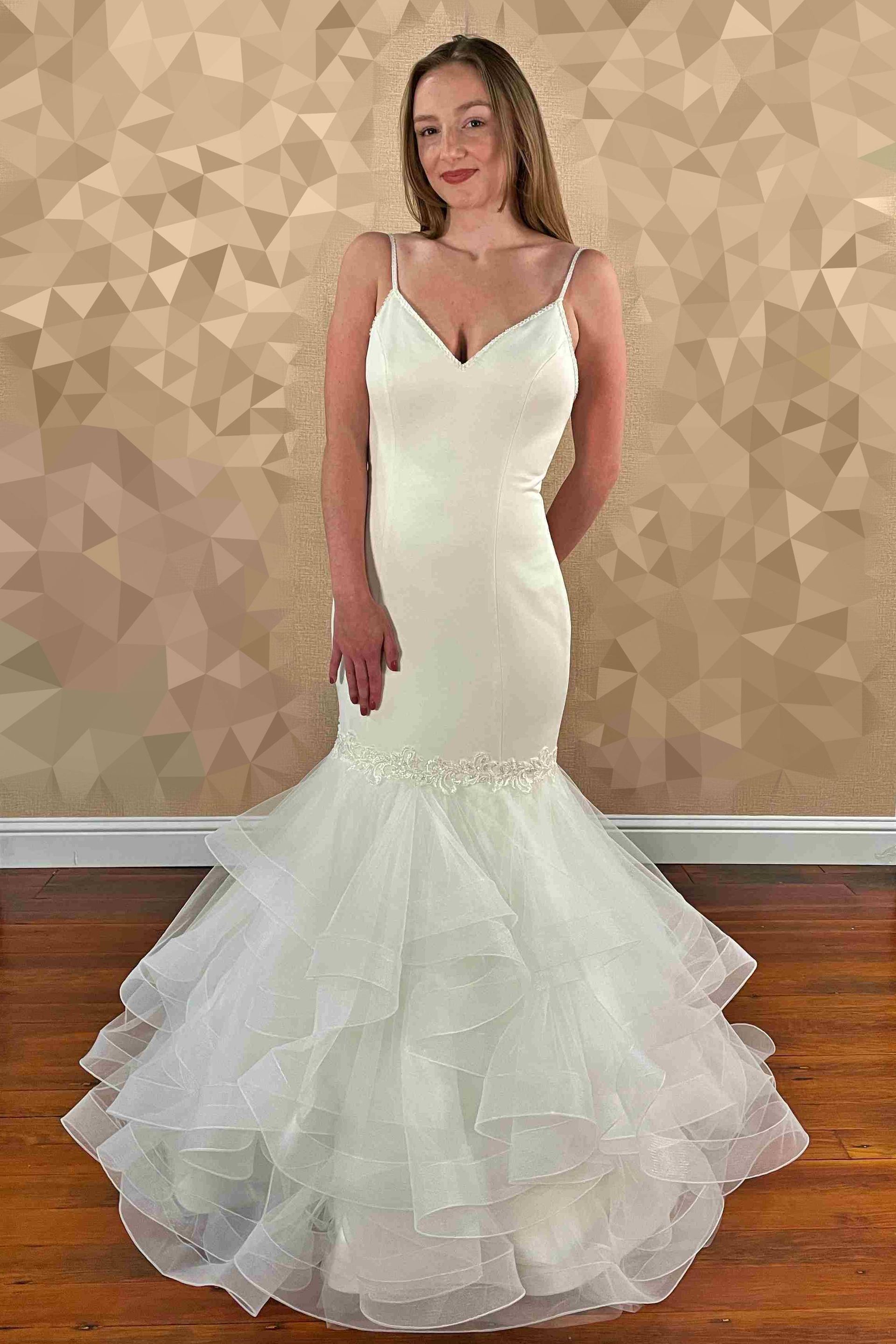 Woman in white wedding dress with spaghetti straps and ruffled skirt.