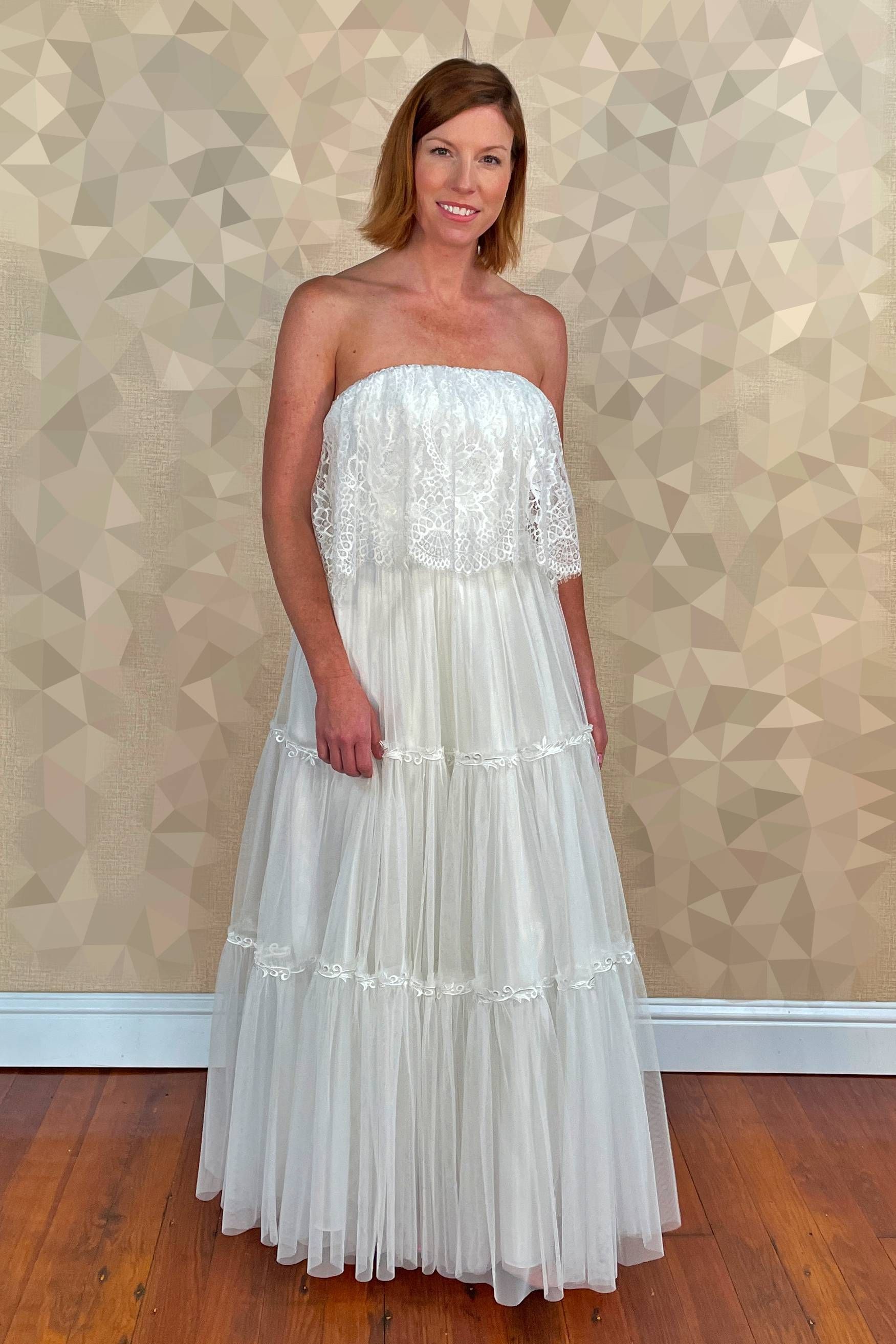 Woman in a white strapless layered dress poses in front of a patterned wall.