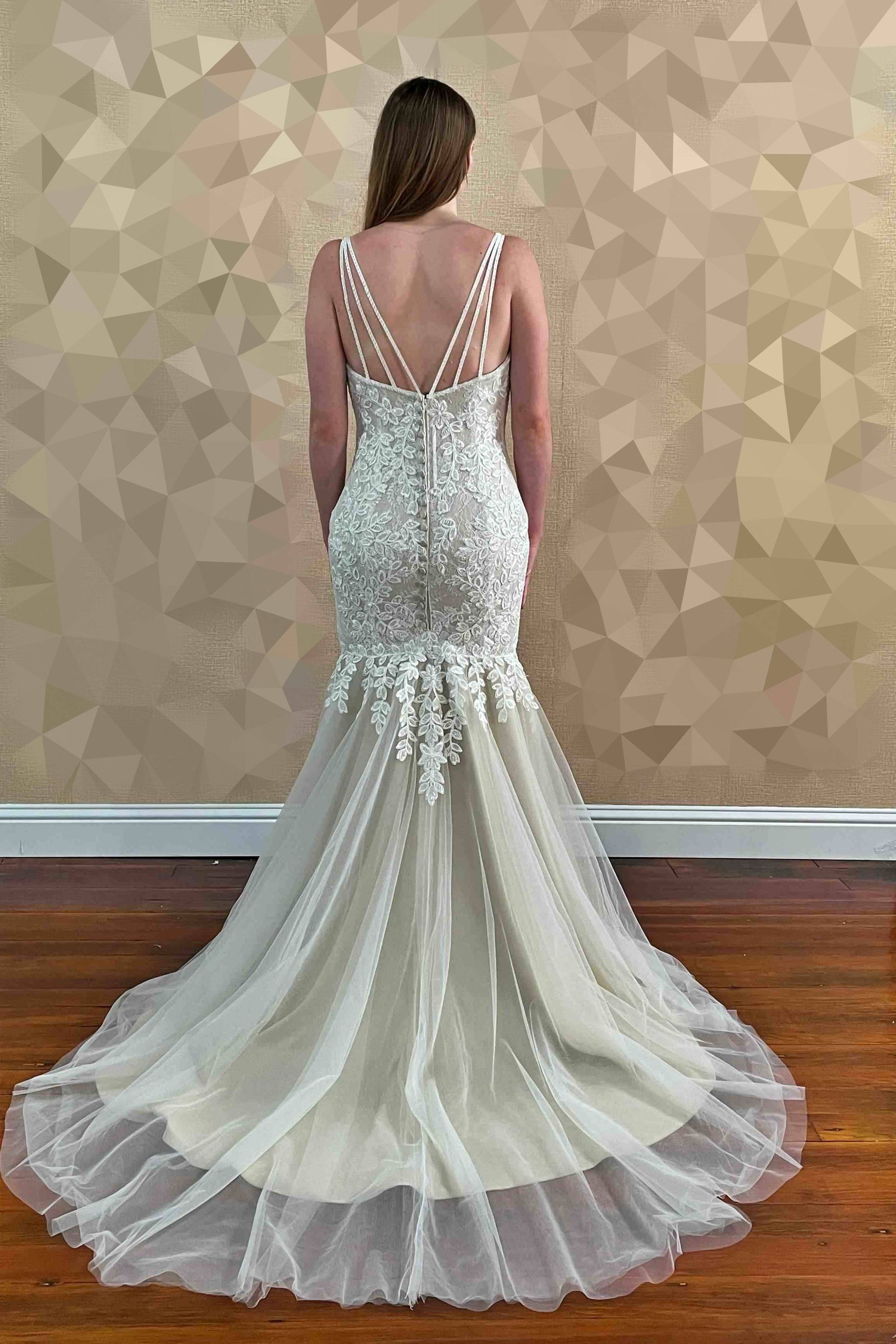 Woman in wedding dress, back view, standing indoors; cream gown with intricate beading and a long, flowing train.