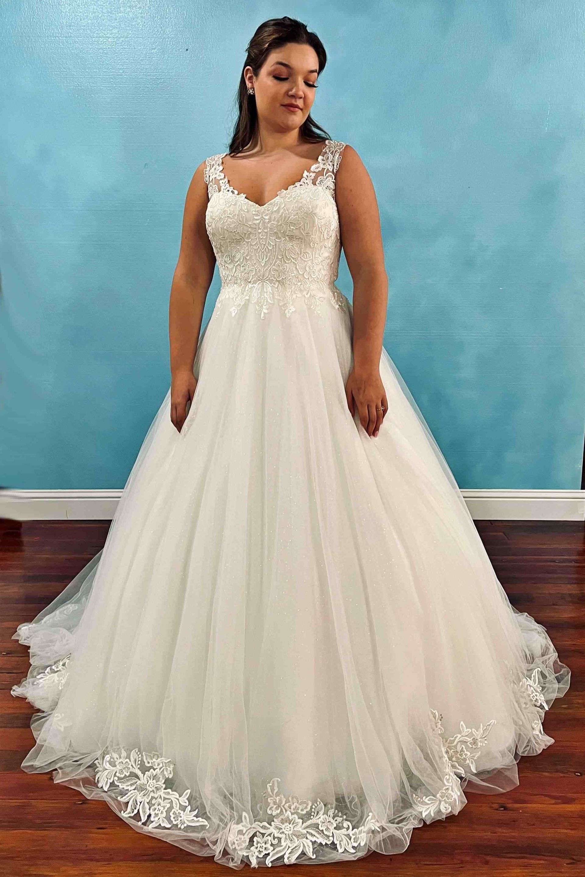 Woman in a white wedding gown with beaded bodice and tulle skirt. Standing indoors against a blue wall.