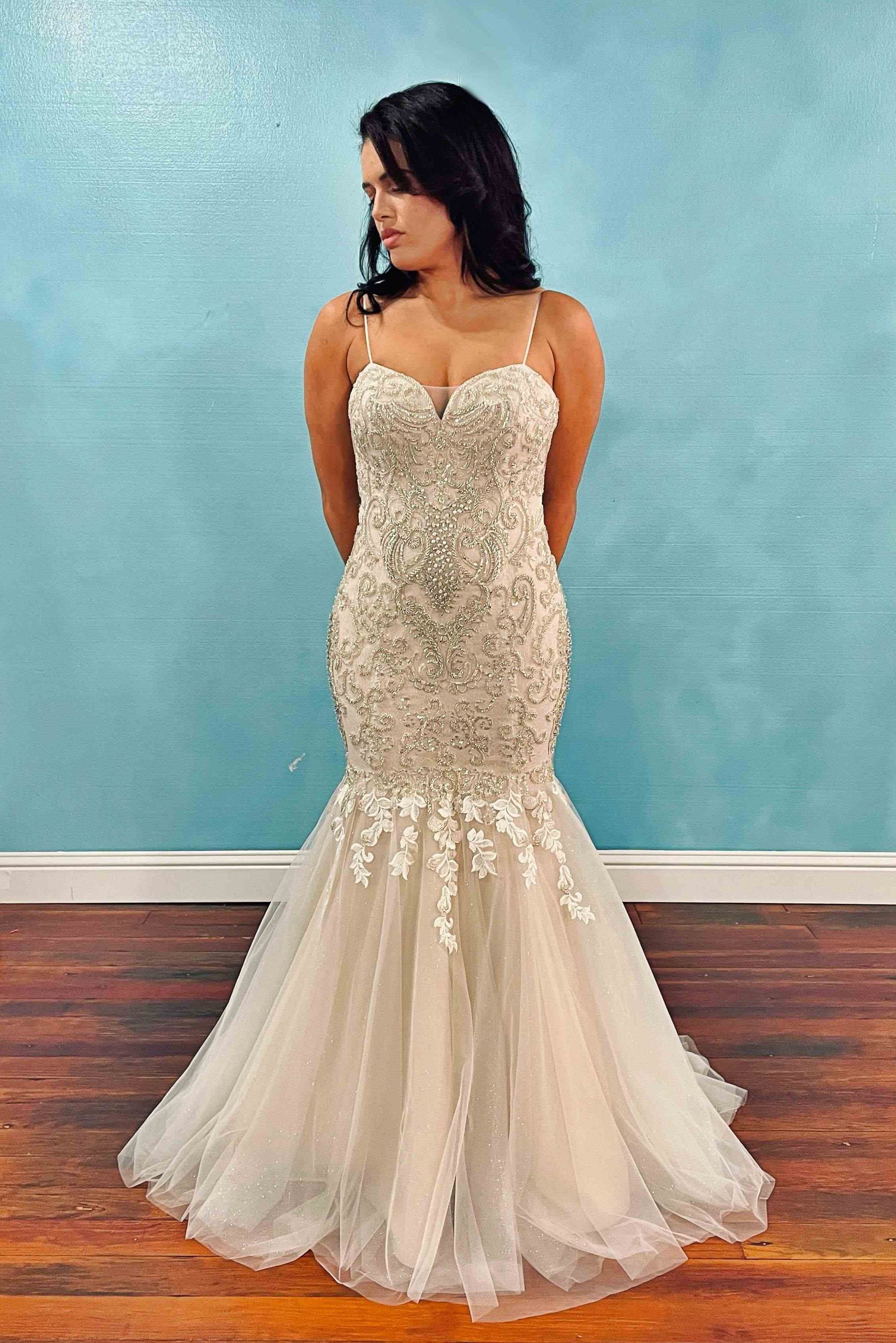 Woman in a beaded mermaid gown with a sweetheart neckline, standing in front of a blue wall.