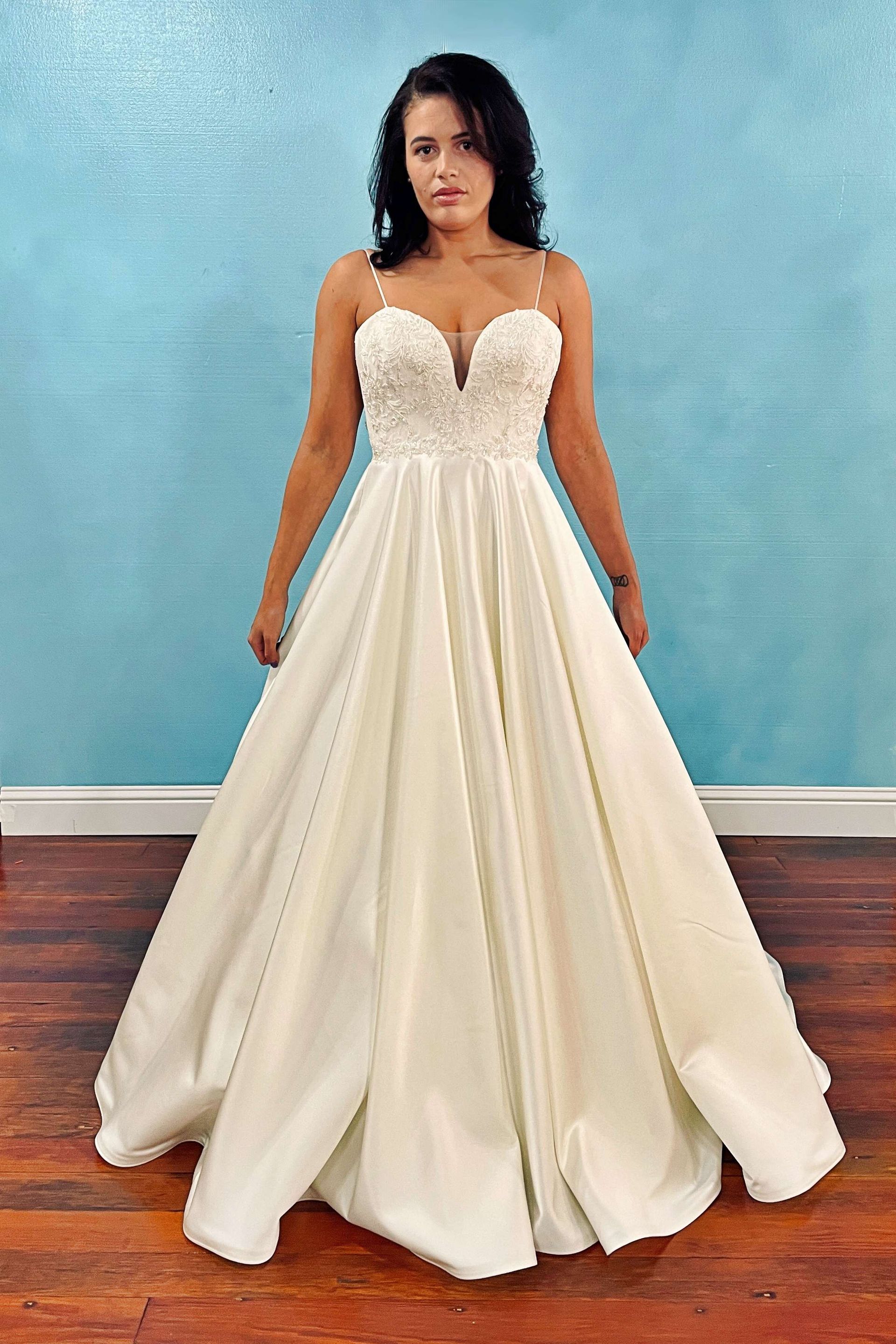Woman in cream-colored ballgown with embellished bodice stands in front of a blue wall.
