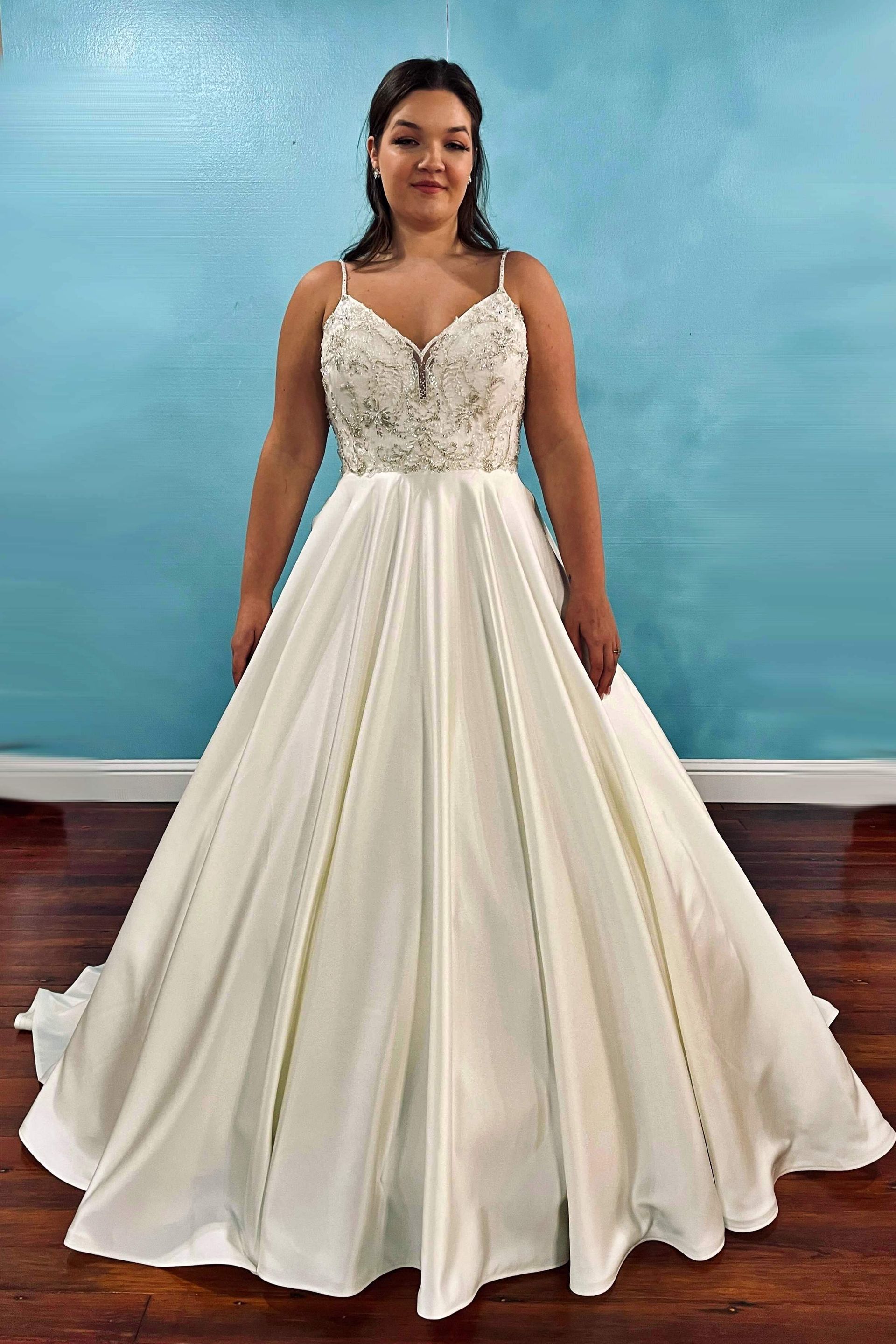 Woman in a white wedding dress with a beaded bodice and flowing skirt, standing in a room.