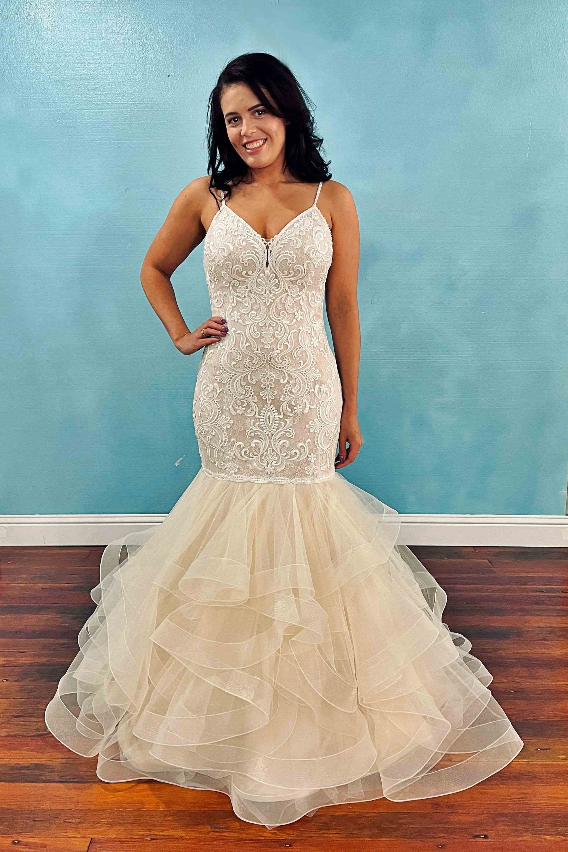 Woman in a sparkly, cream-colored mermaid wedding dress, standing with hand on hip.
