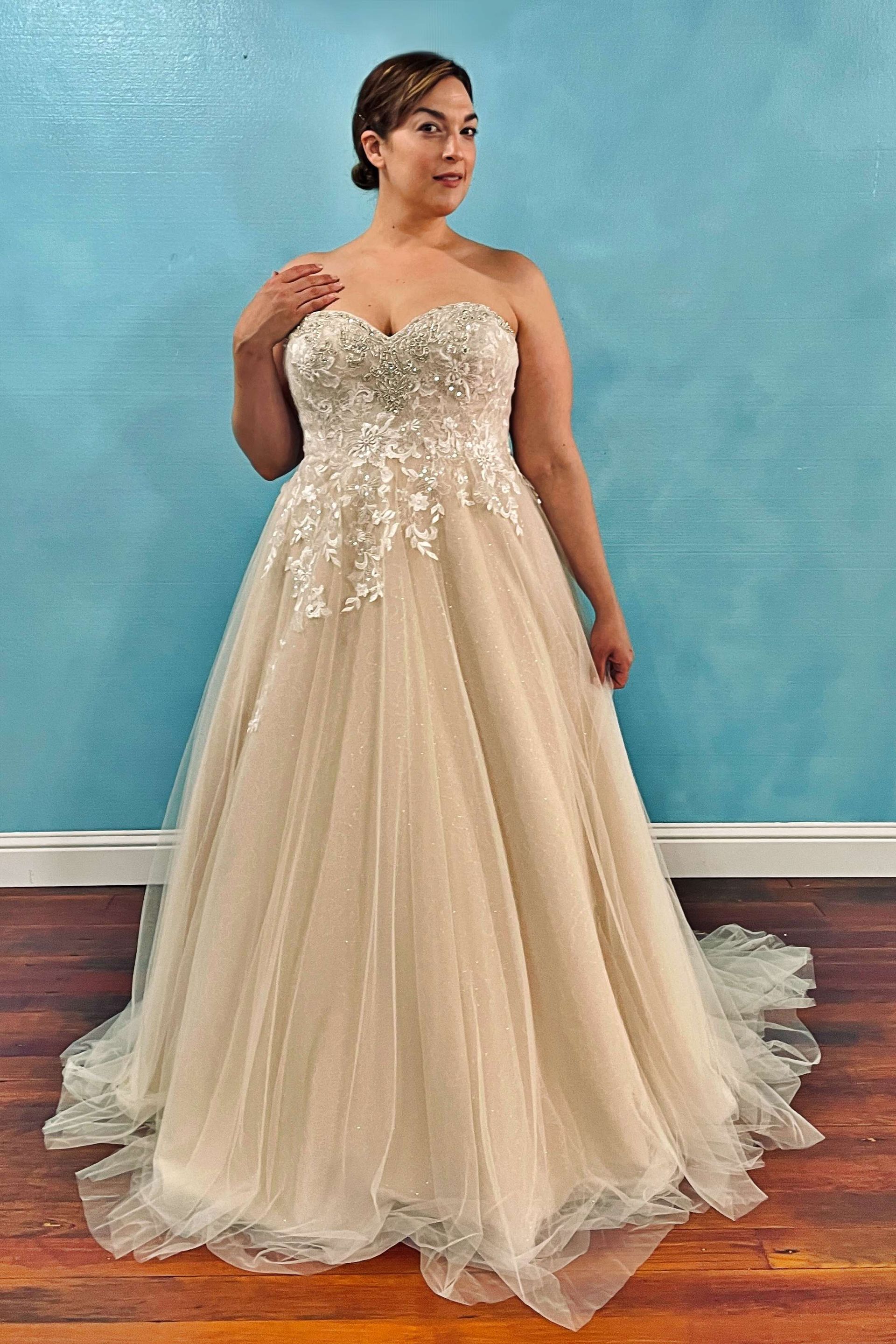Woman in a strapless ivory wedding dress with embellished bodice, standing in a bridal shop.