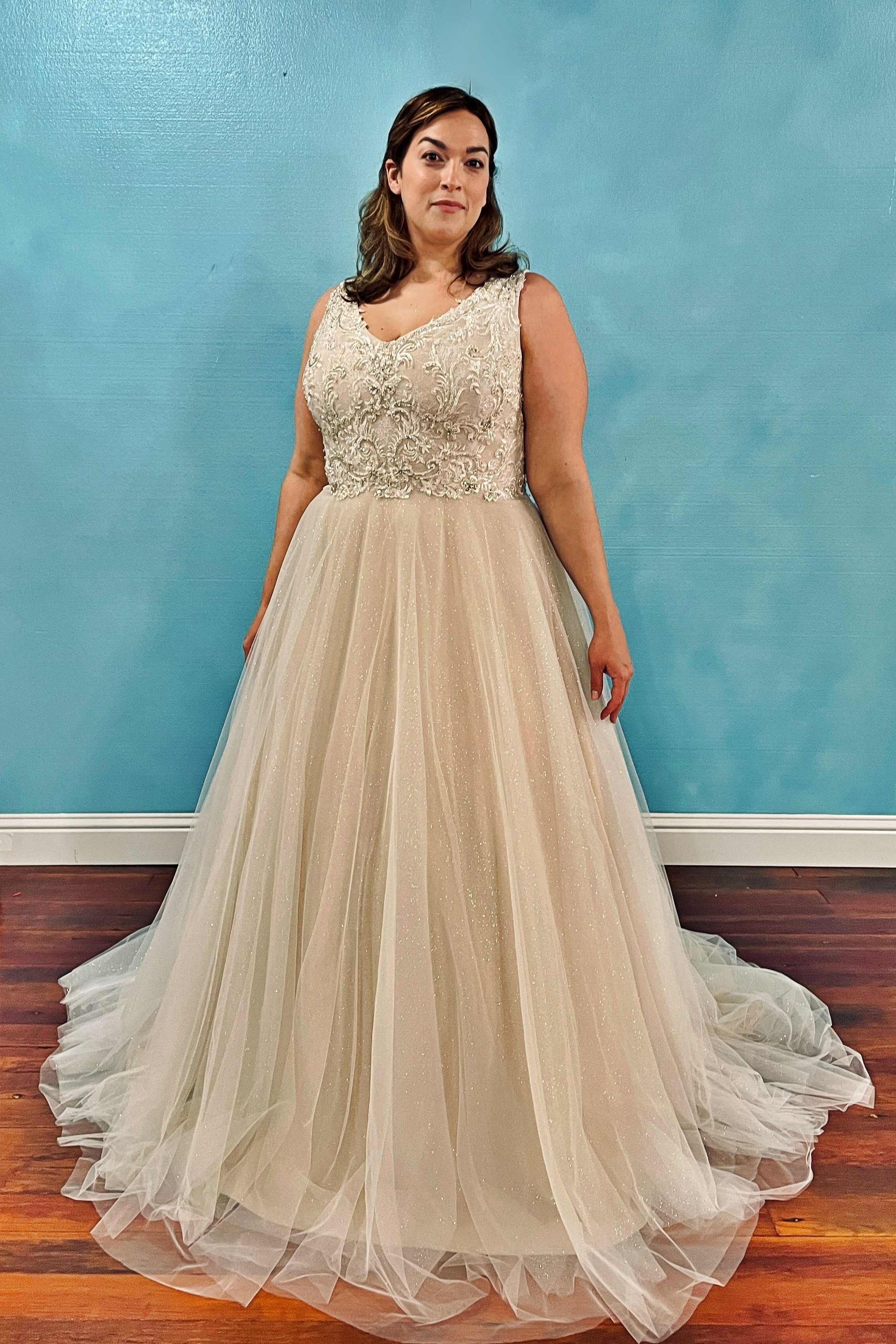 Woman in a sparkling, beaded wedding dress poses in front of a blue wall.