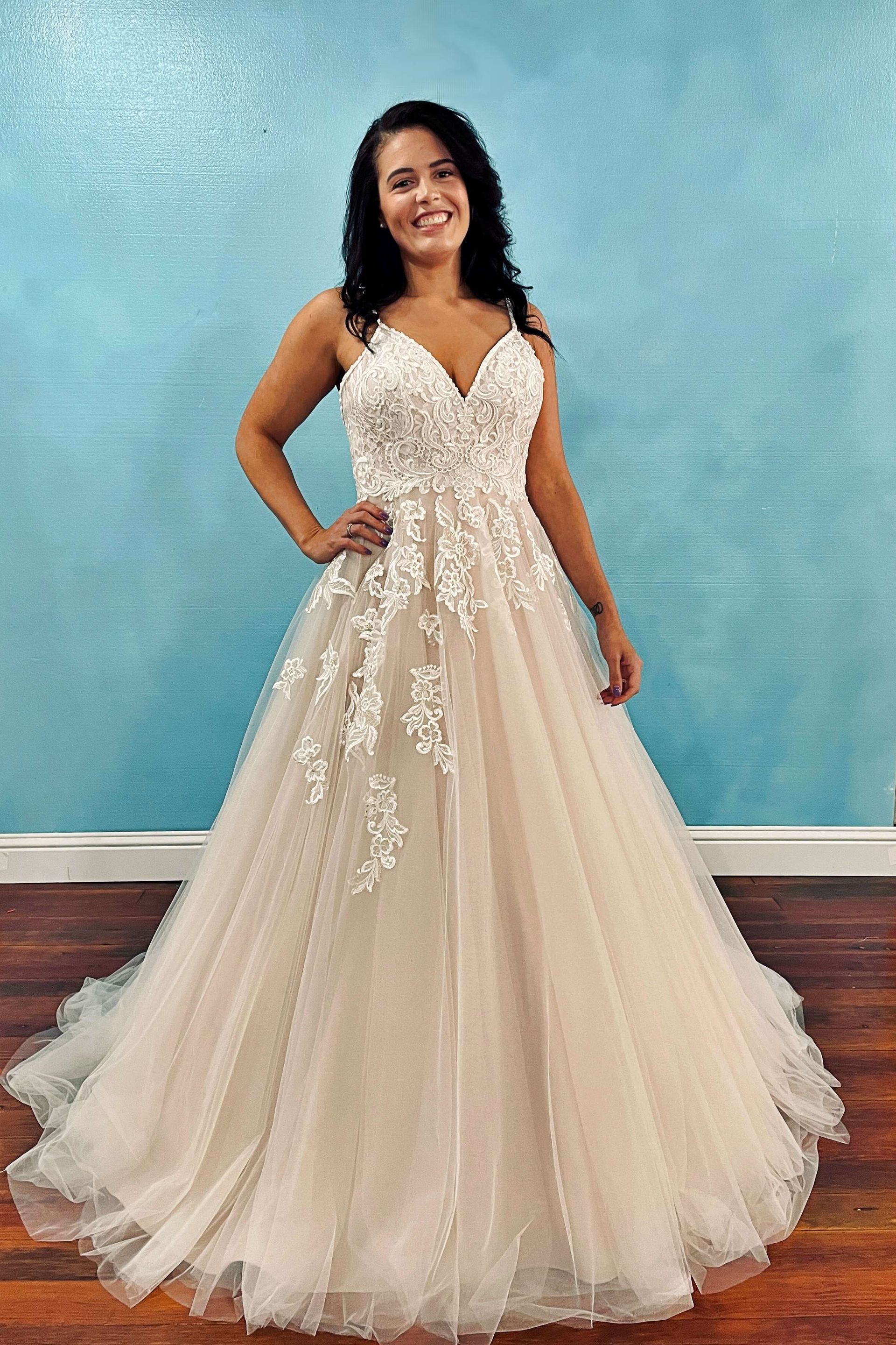 Woman in a light-colored wedding dress, posing indoors with a blue wall backdrop.