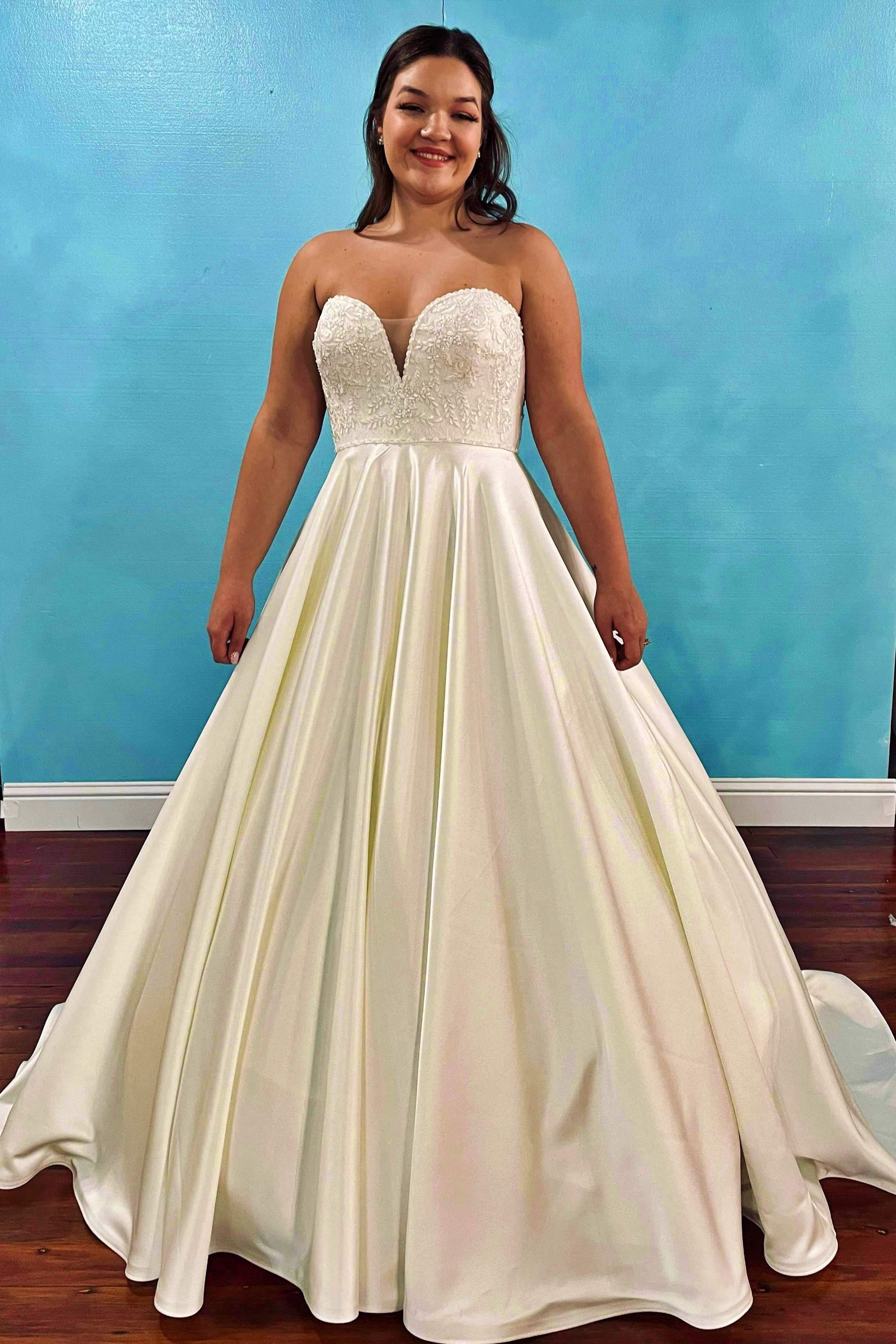 Woman in strapless wedding dress with beaded bodice, standing in front of blue wall.