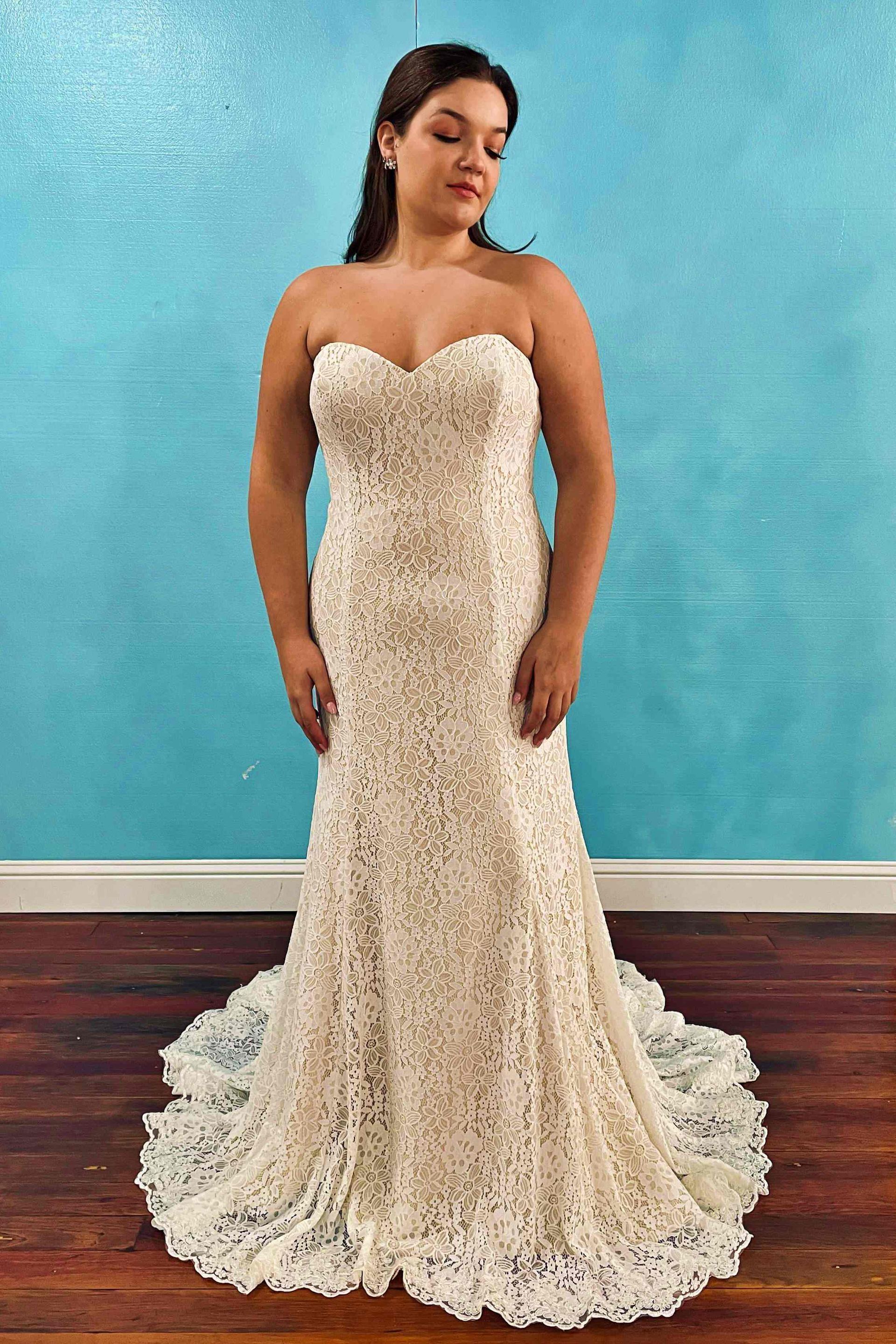 Woman in a strapless ivory lace wedding dress, mermaid style, standing in front of a blue wall.