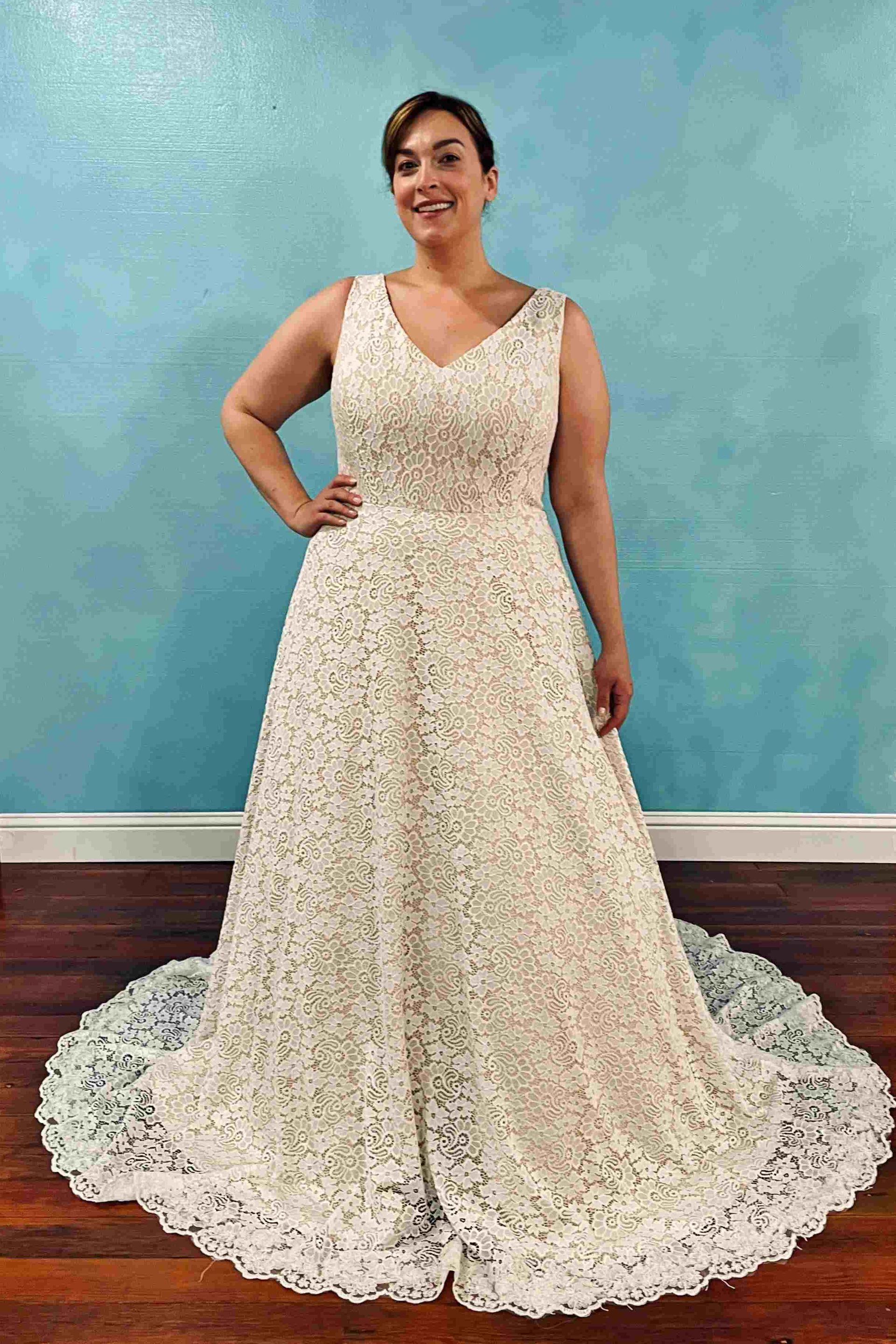 Woman in a white lace wedding dress, smiling, posing in front of a blue wall.