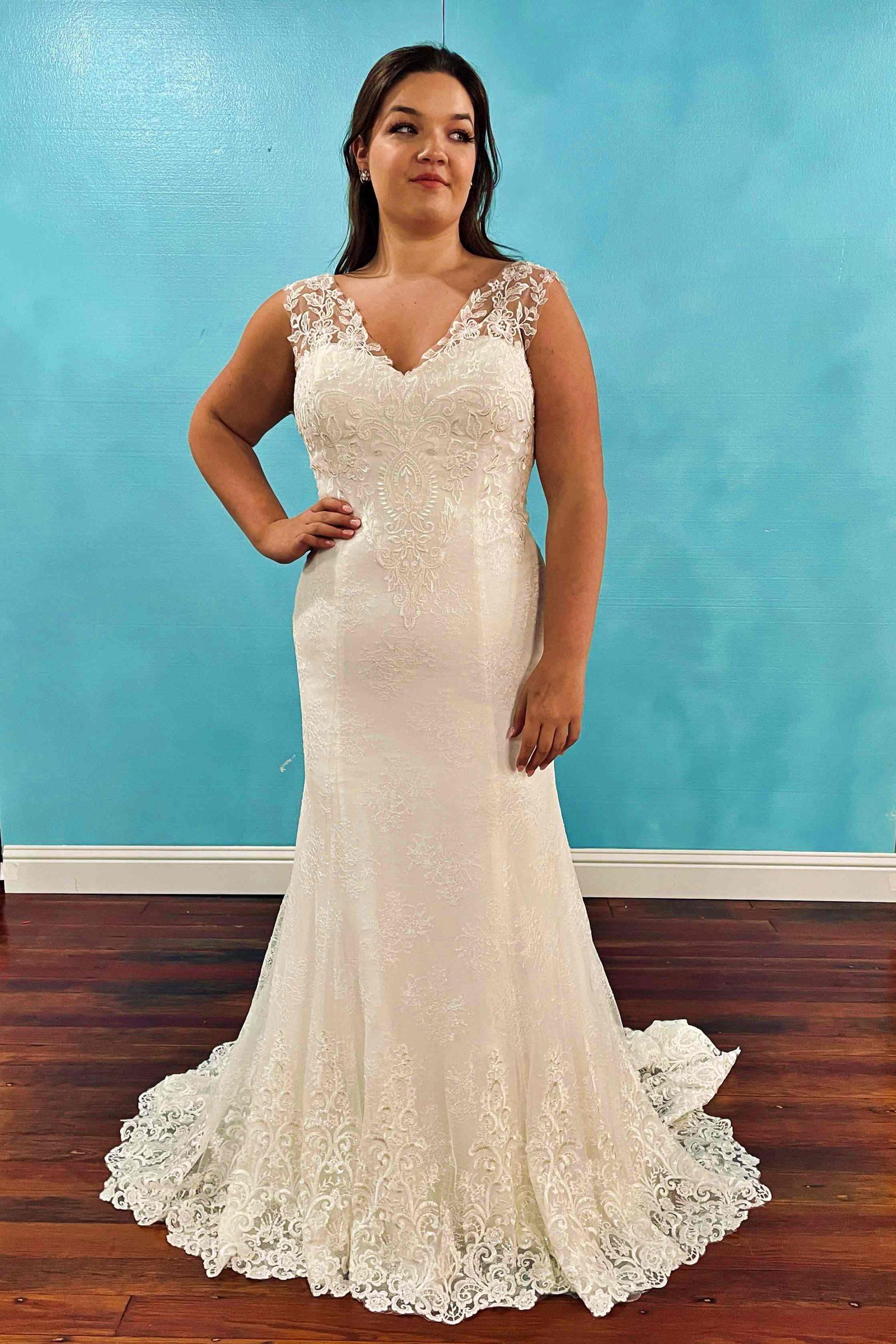 Woman in a white lace mermaid wedding dress poses in front of a blue wall.