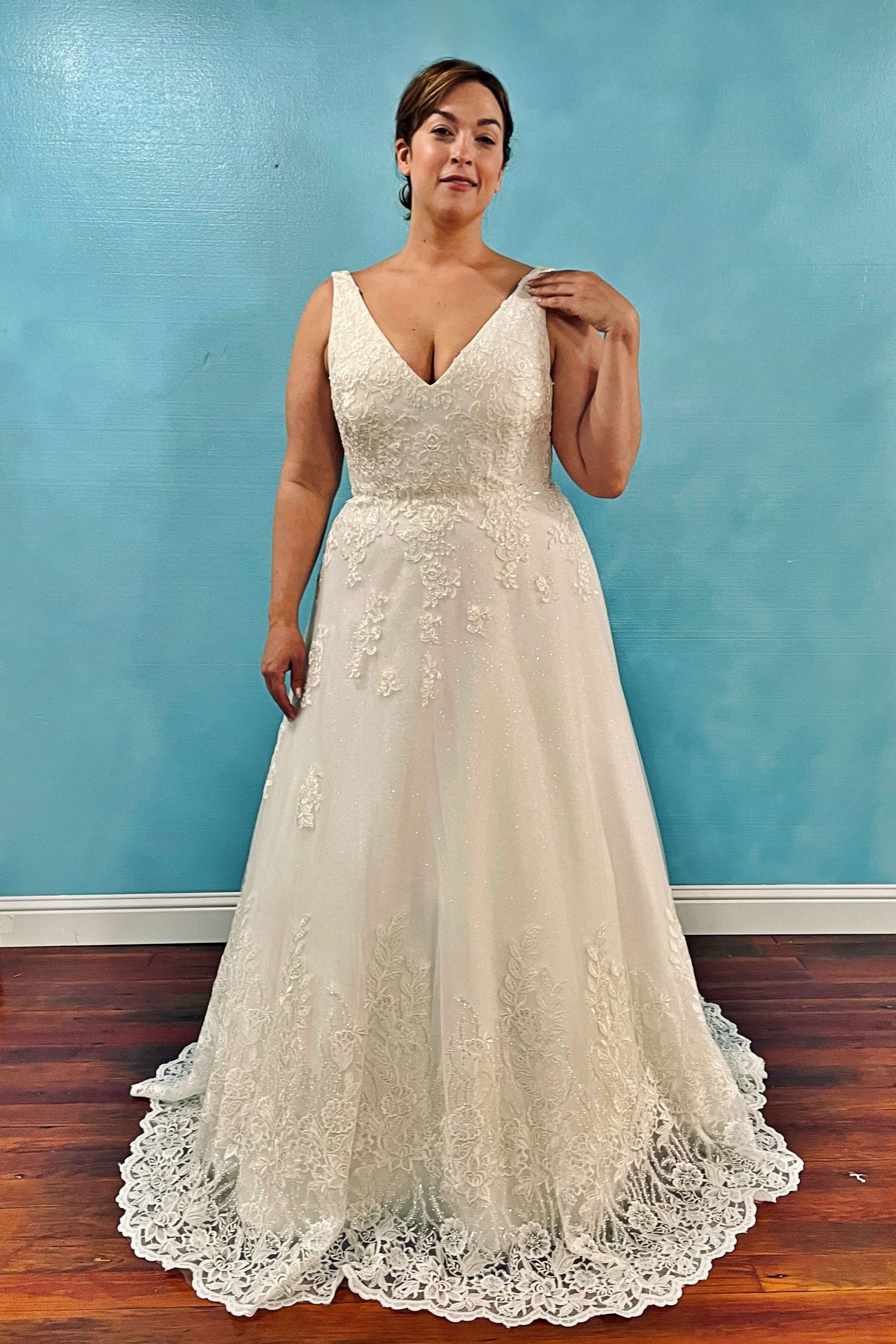 Woman in a white beaded wedding dress with a V-neckline stands against a blue wall.
