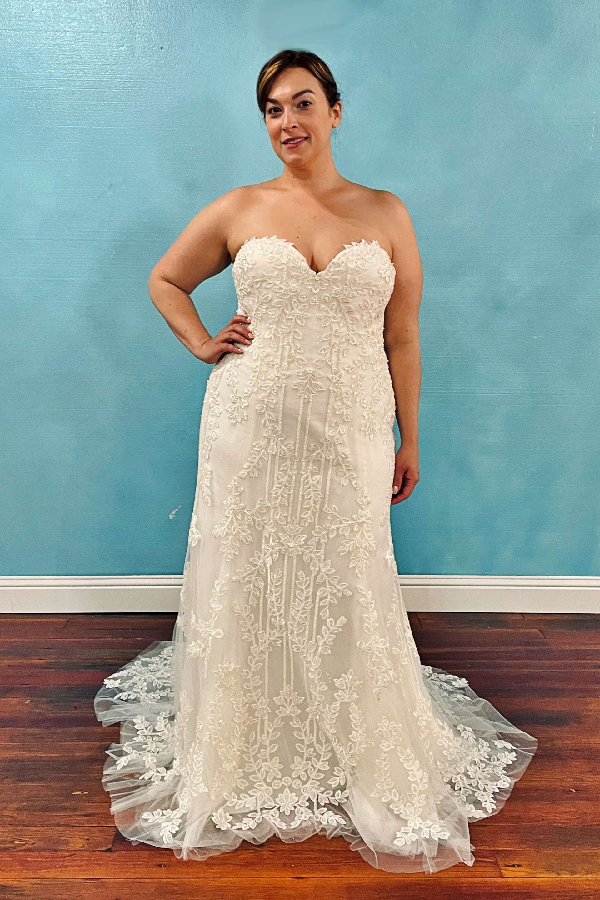 Woman in a strapless ivory wedding gown with beaded embellishments, smiling and posing in front of a blue wall.