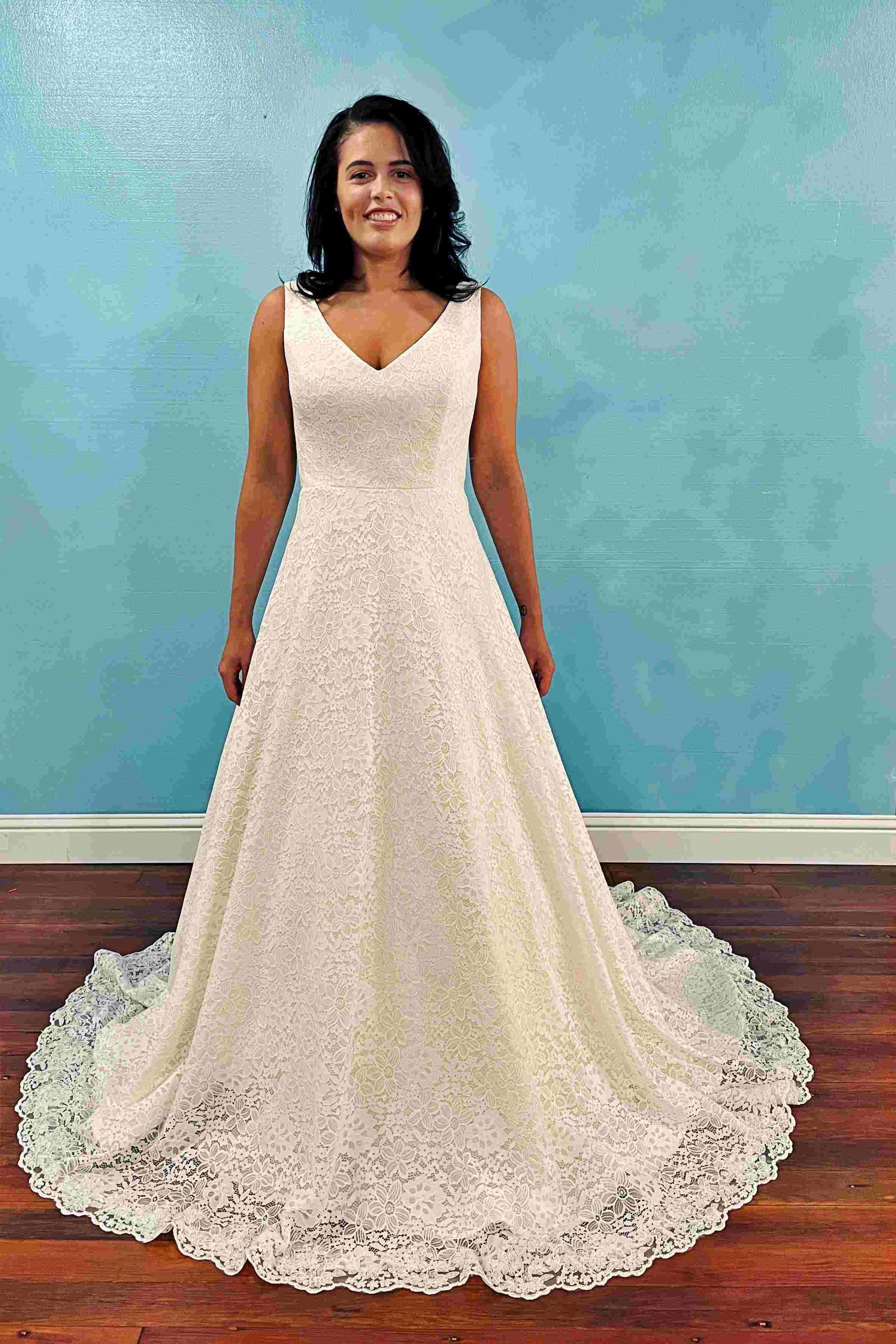Woman in a white lace wedding dress, smiling, in front of a blue wall.