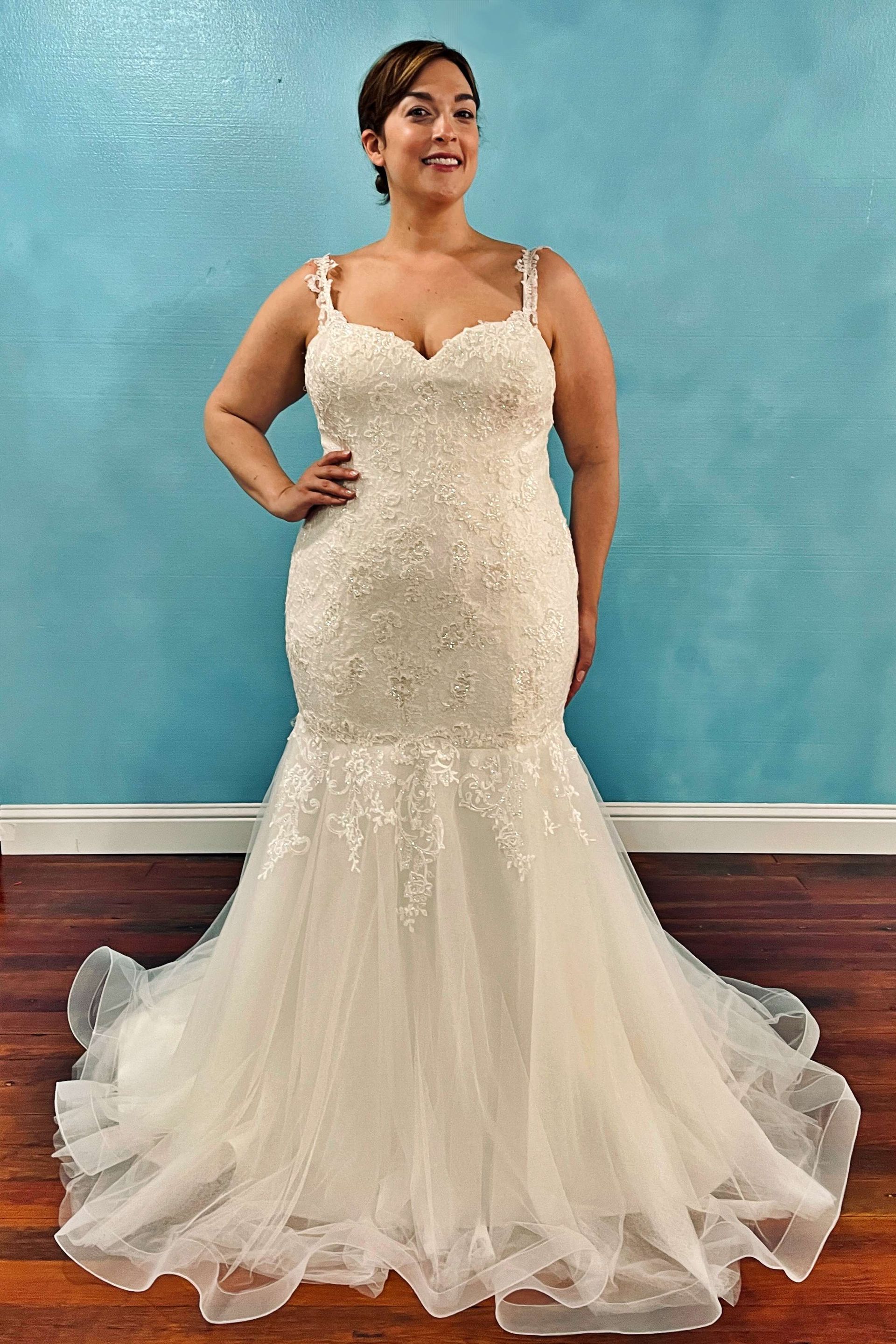 Woman in a white beaded mermaid wedding dress, standing in front of a blue wall, smiles.