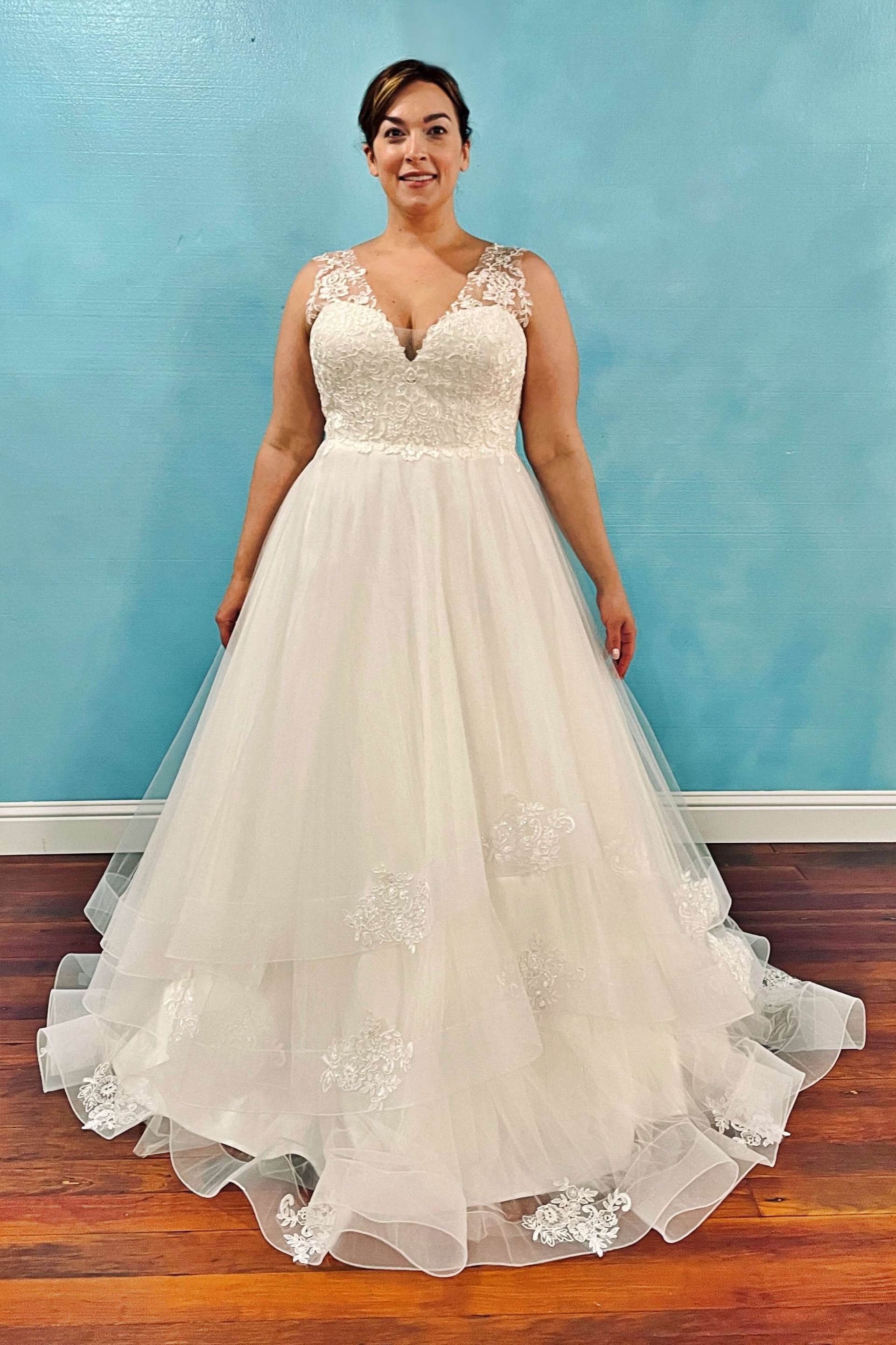 Woman in a white wedding dress with a V-neck and lace details, standing in front of a blue wall.