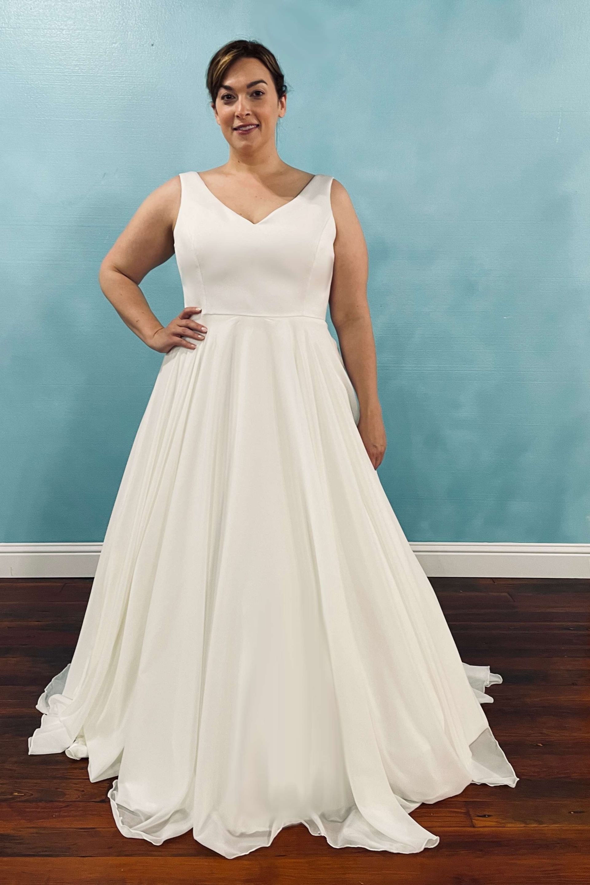 Woman in white wedding dress with a V-neck, standing in front of a blue wall.
