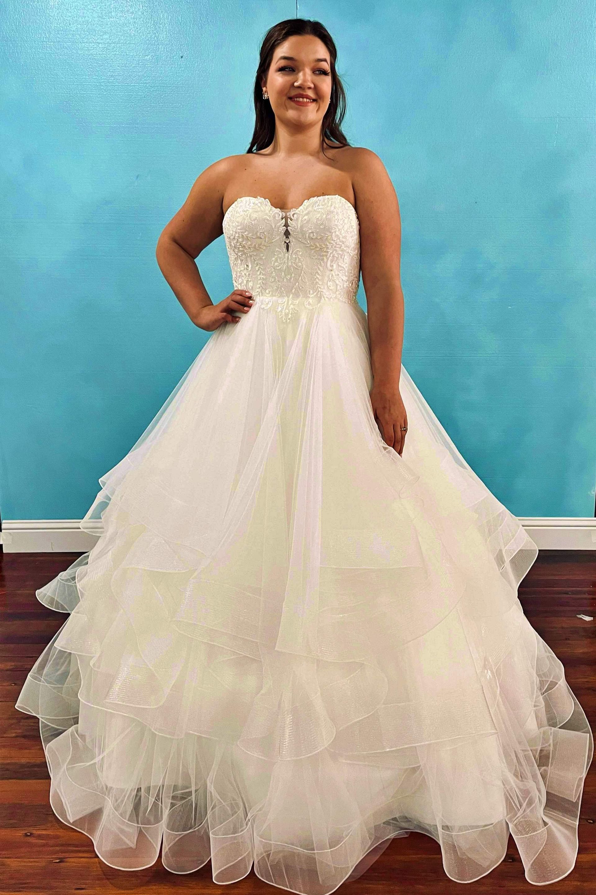Woman in a white strapless ballgown with beaded bodice, smiling, standing in front of a blue wall.