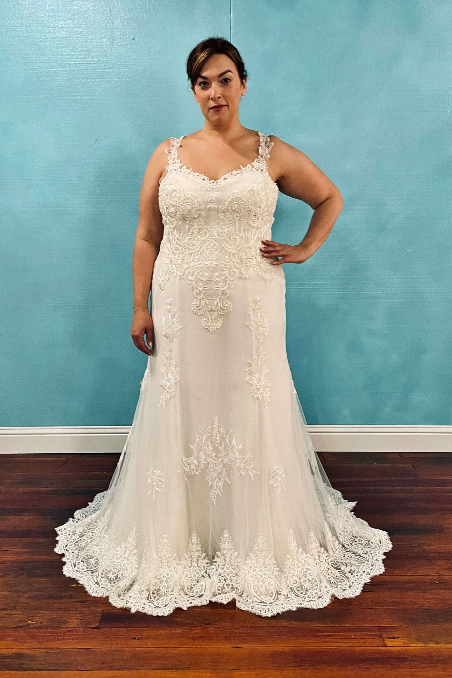 Woman in a white beaded wedding dress with lace detail, poses with hand on hip.
