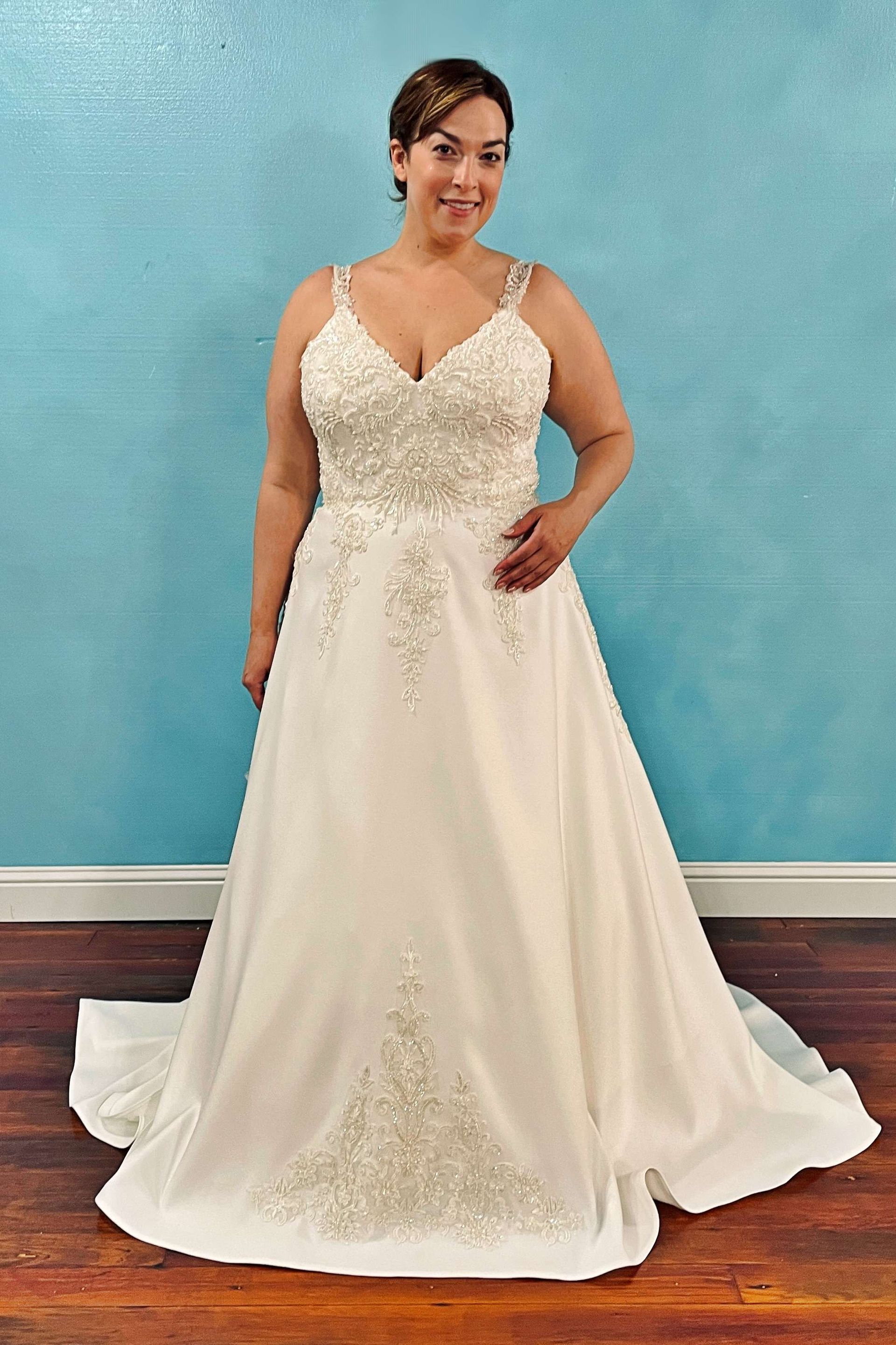 Woman in a white wedding dress with beaded bodice, standing in front of a blue wall.