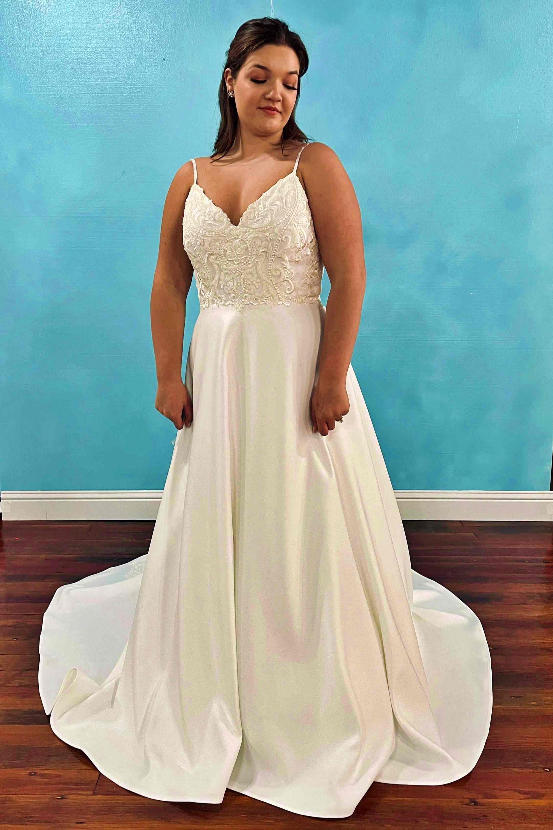 Woman in a white wedding dress with a beaded bodice and flowing skirt, standing in front of a blue wall.
