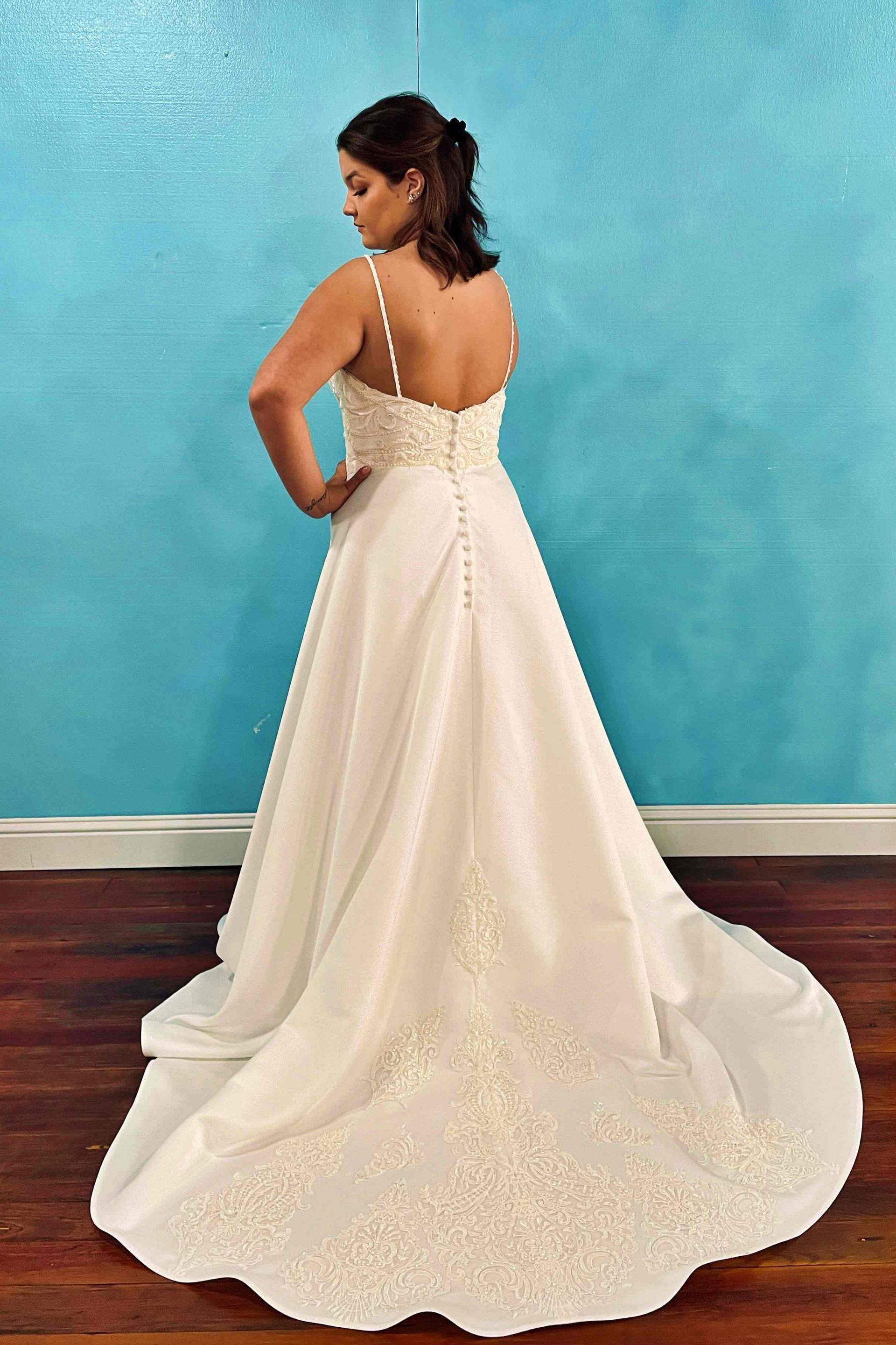 Woman in wedding dress, back view, on wooden floor against a blue wall. Dress with beaded bodice, spaghetti straps