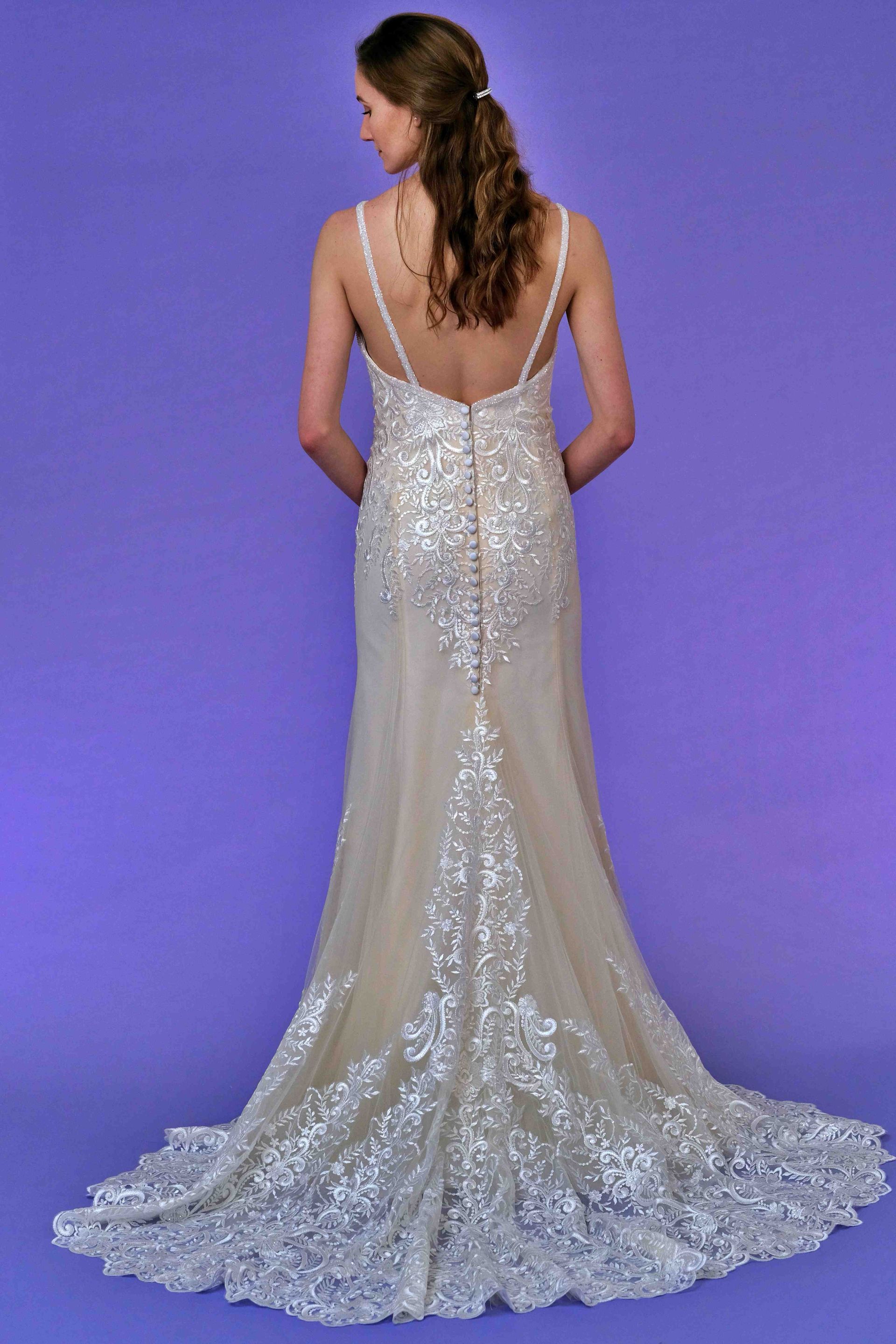Woman in a sequined wedding dress, back view, low back, long train, against a purple backdrop.