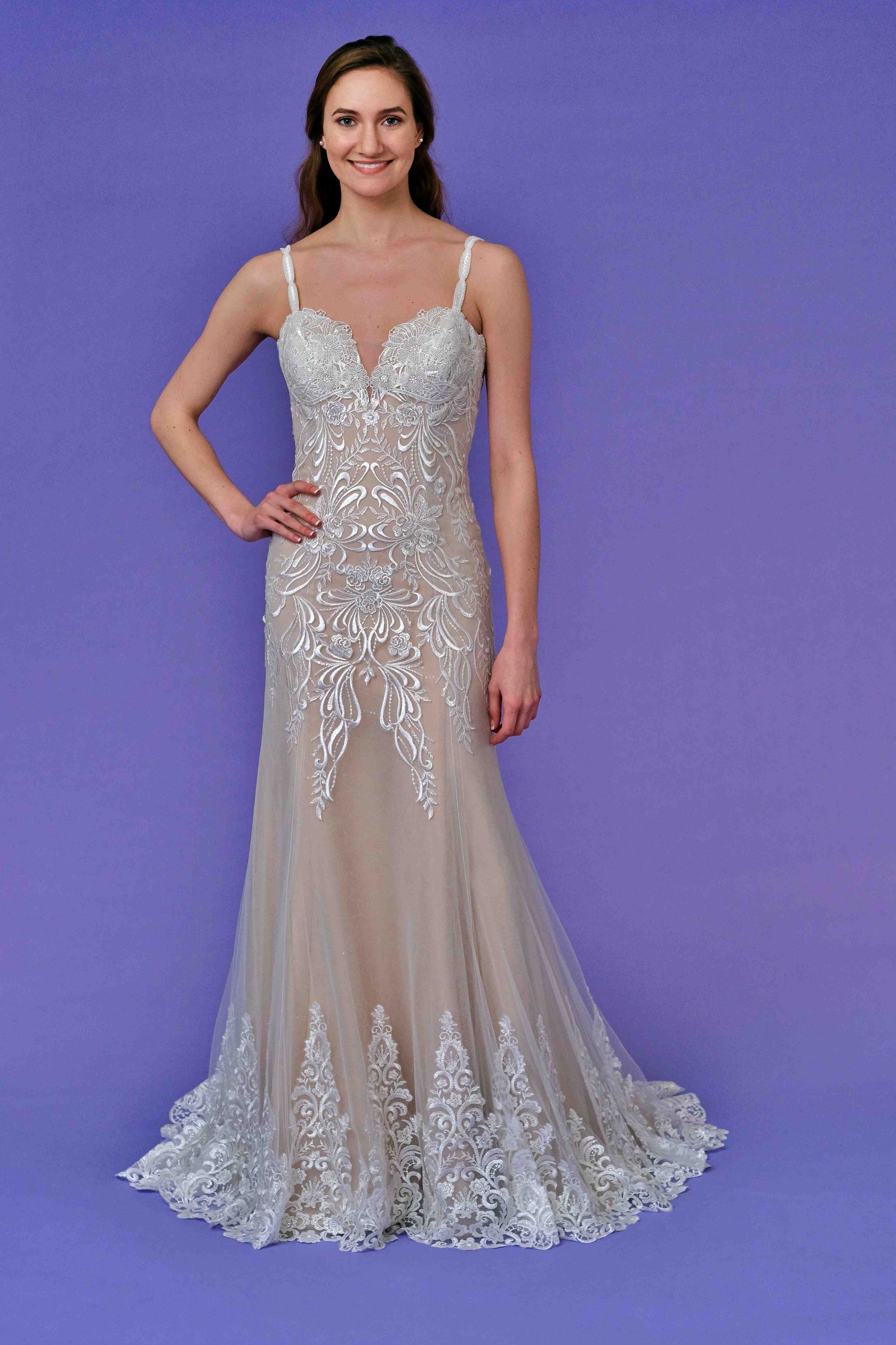 Woman wearing a shimmering, silver-beaded gown with spaghetti straps, posing in front of a purple background.