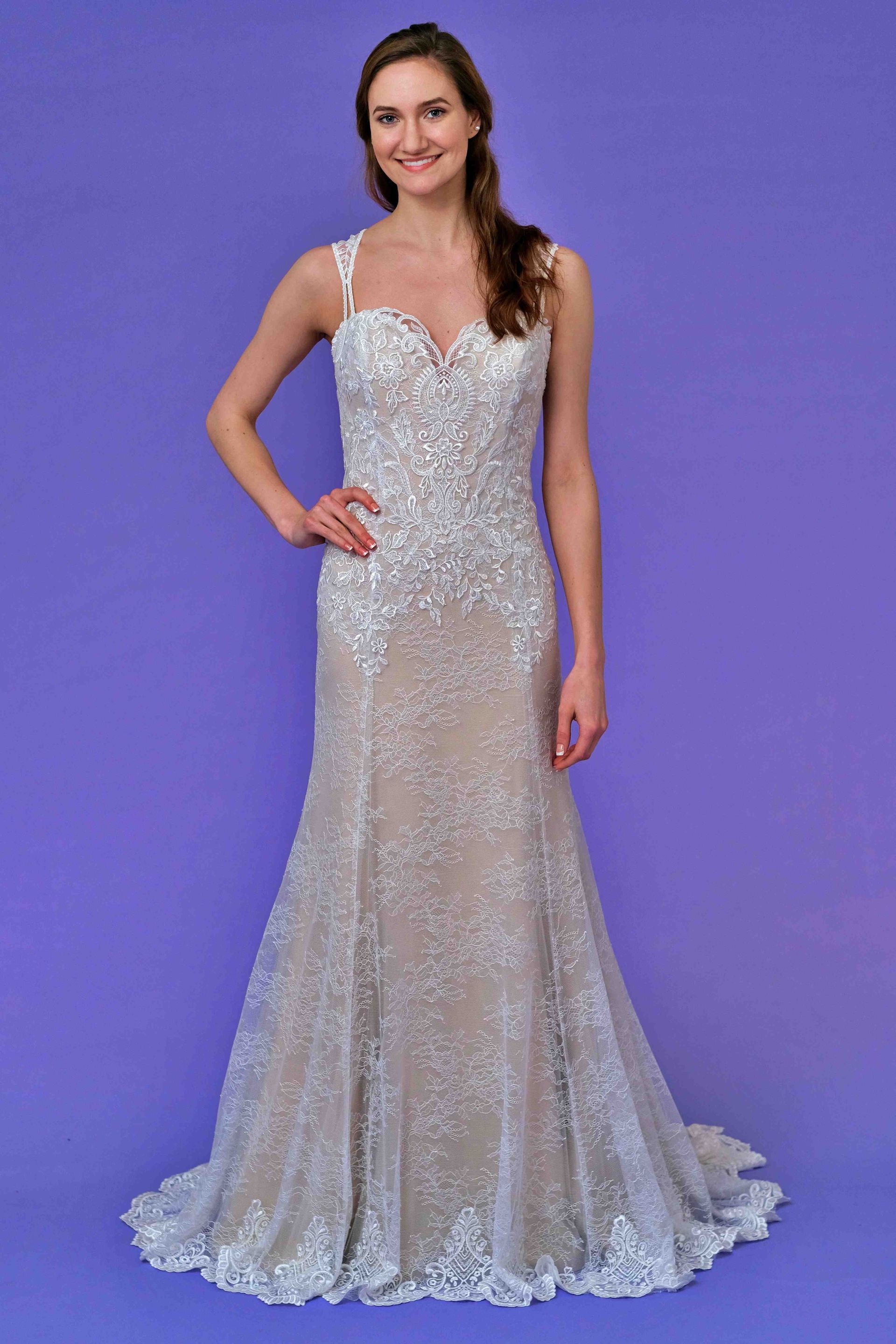 Woman in a sparkling, fitted wedding gown with a train, poses in front of a purple background.