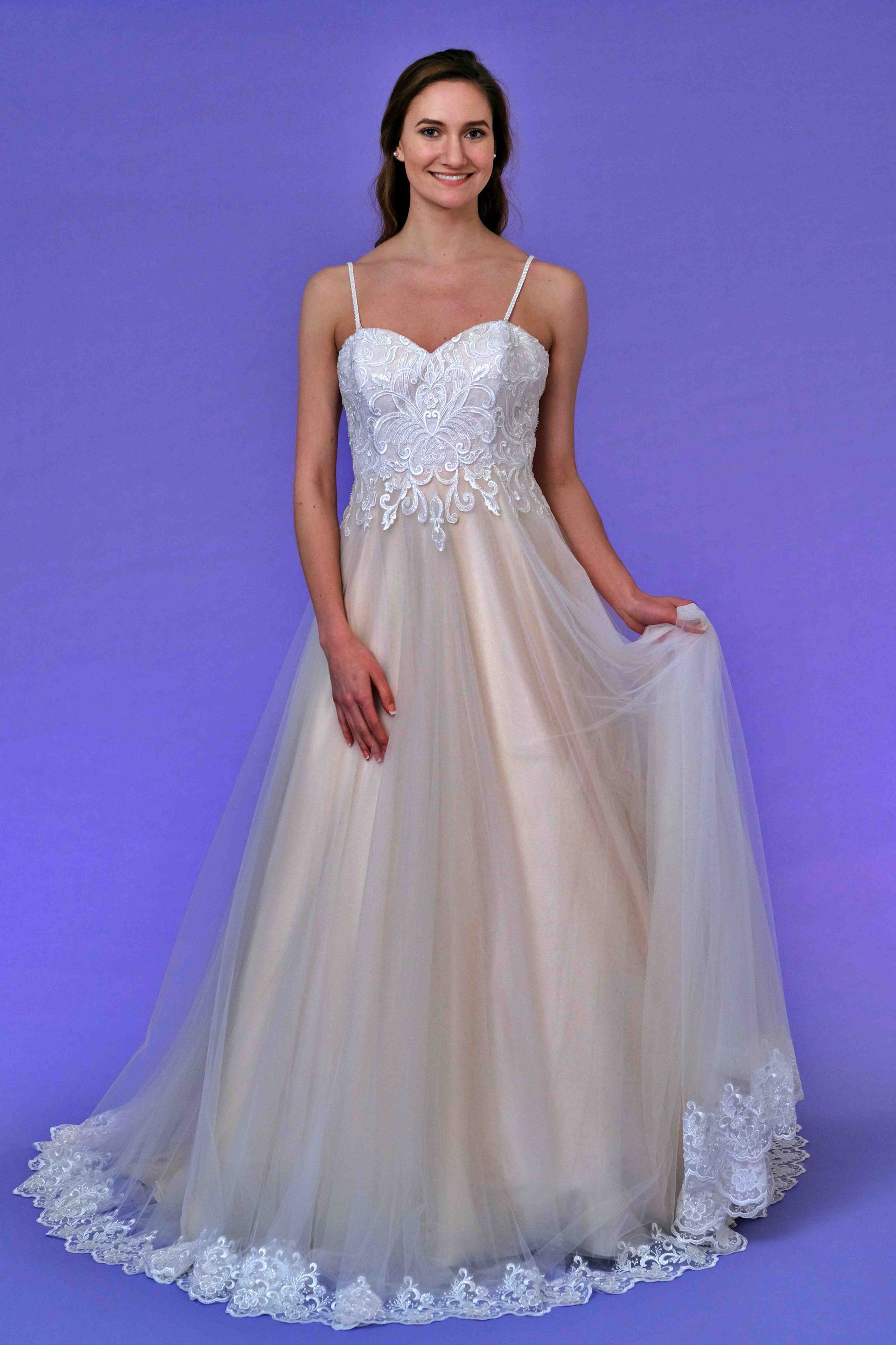 Woman in a white wedding gown, smiling, holding skirt, in front of a purple backdrop.