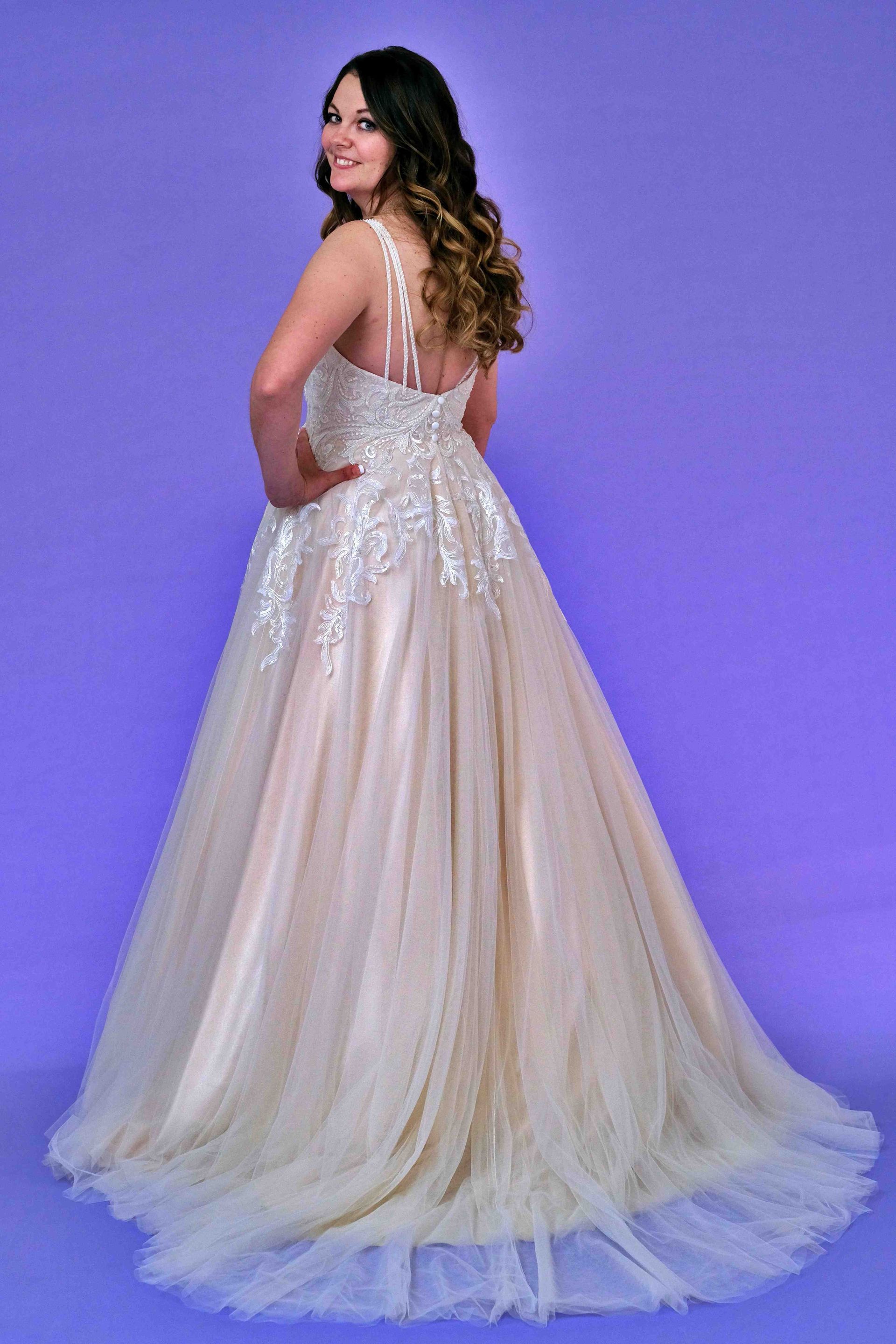 Woman in a formal gown with spaghetti straps, looking over her shoulder, on a purple background.