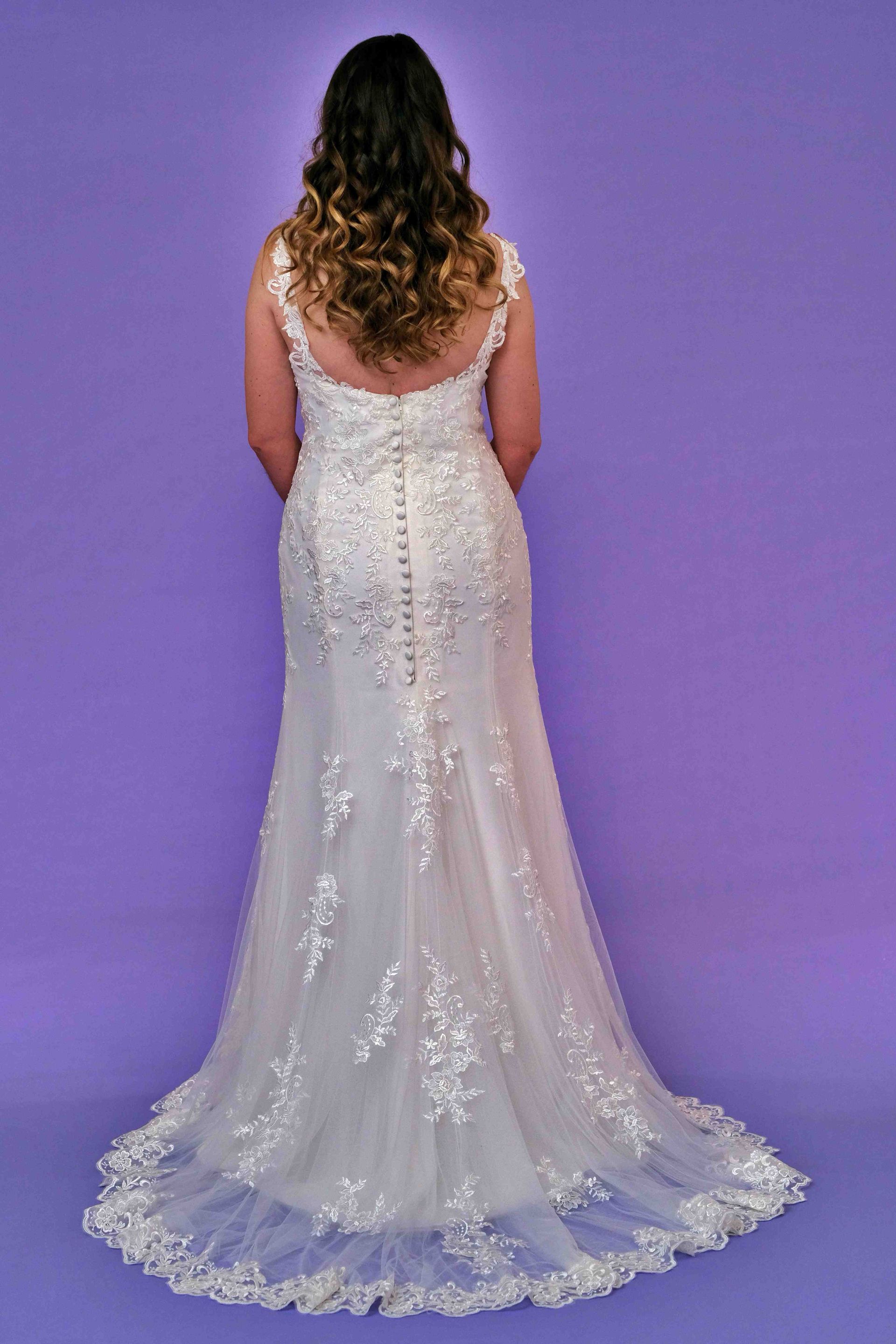 Woman in a white wedding dress with a train, standing against a purple backdrop.