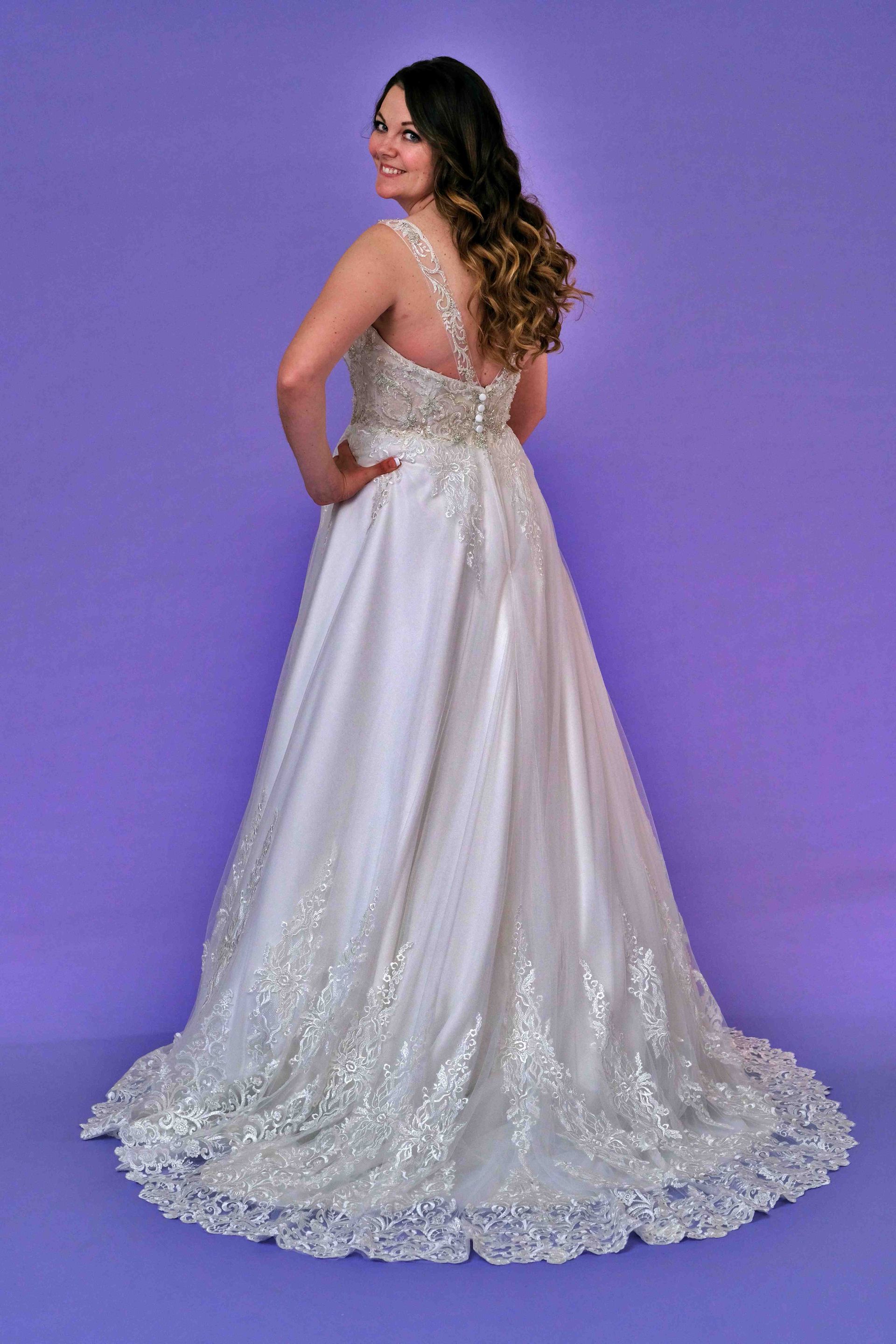 Woman in a white wedding gown, looking over her shoulder, on a purple background.