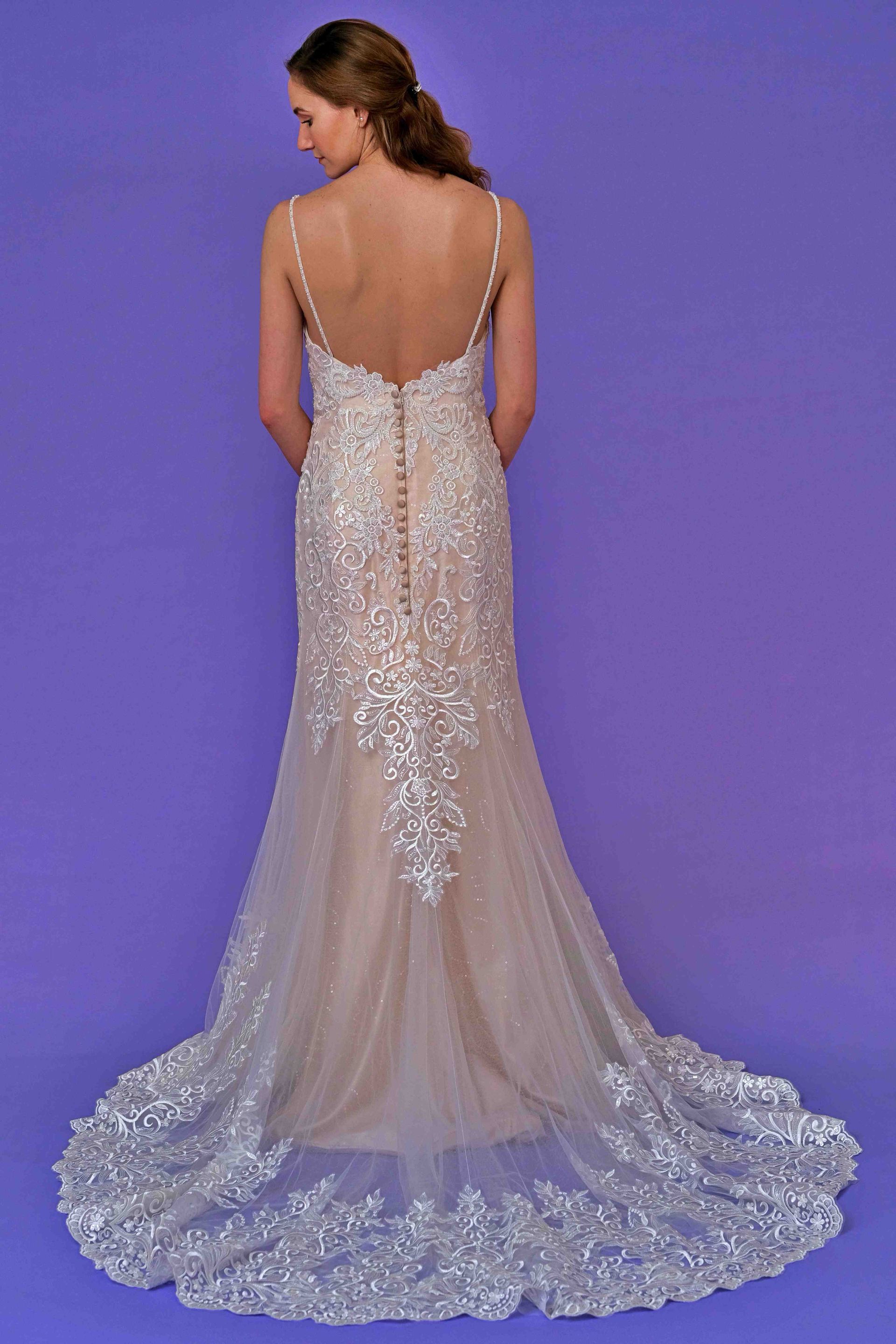 Woman in a beaded, backless gown with a long train, standing against a purple background.