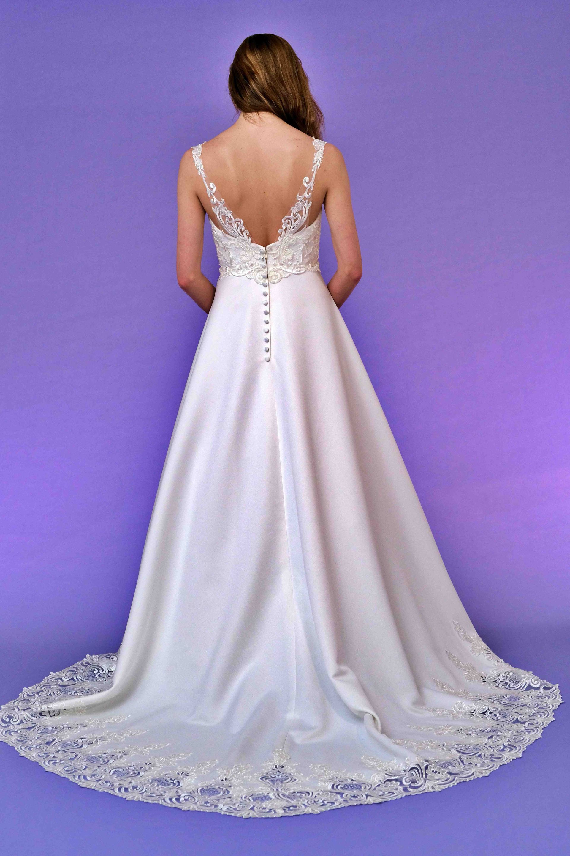 Woman in a white wedding dress with a long train, standing against a purple background.